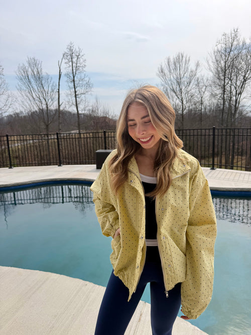 Woman in a yellow jacket standing by a pool with bare trees in the background