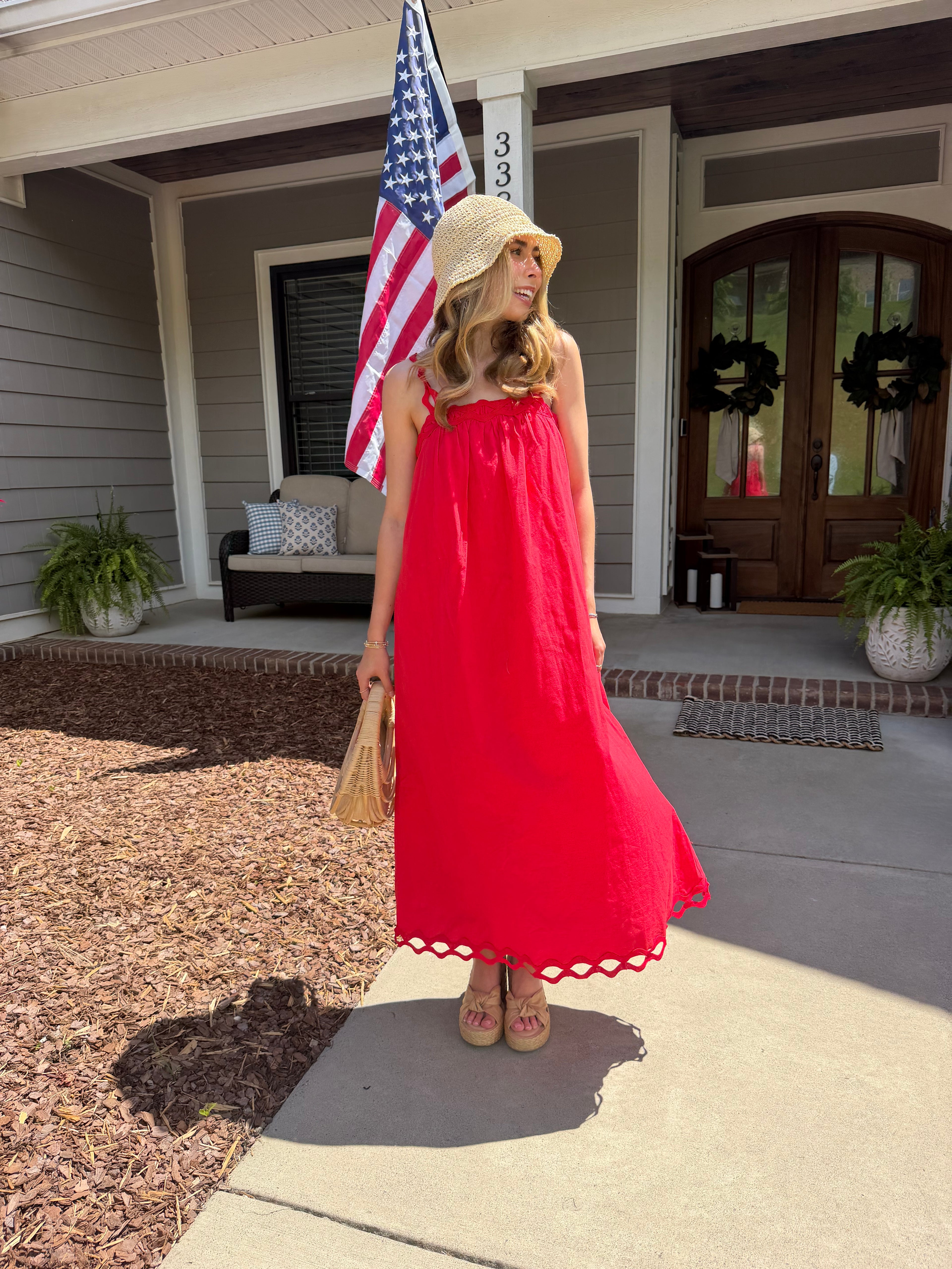Woman in a red dress holding an American flag on a front porch.
