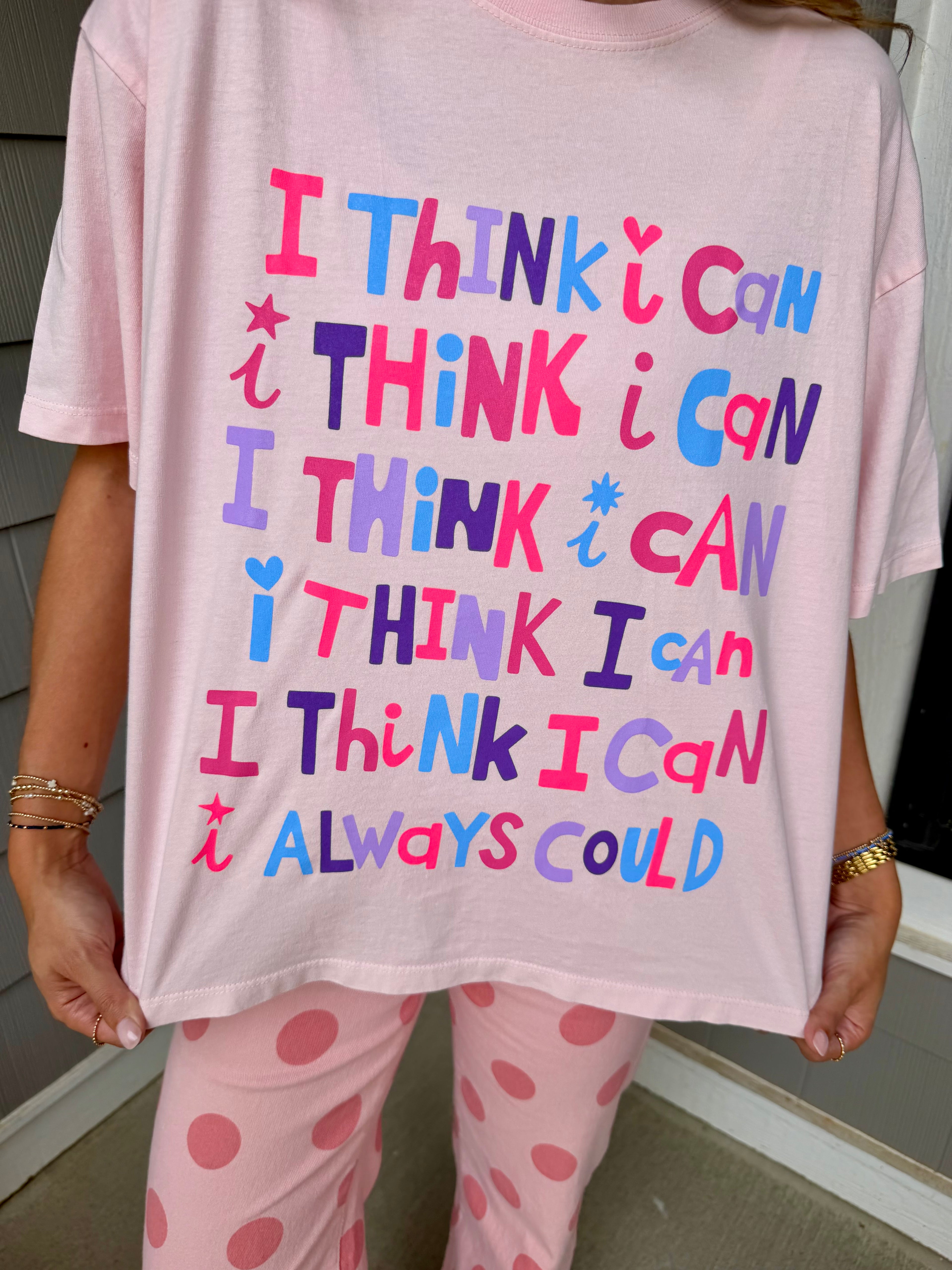 A person wearing a light pink oversized T-shirt with colorful text that reads 'I THINK I CAN I THINK I CAN I THINK I CAN I THINK I CAN I THINK I CAN I ALWAYS COULD' paired with pink polka-dot pajama pants.