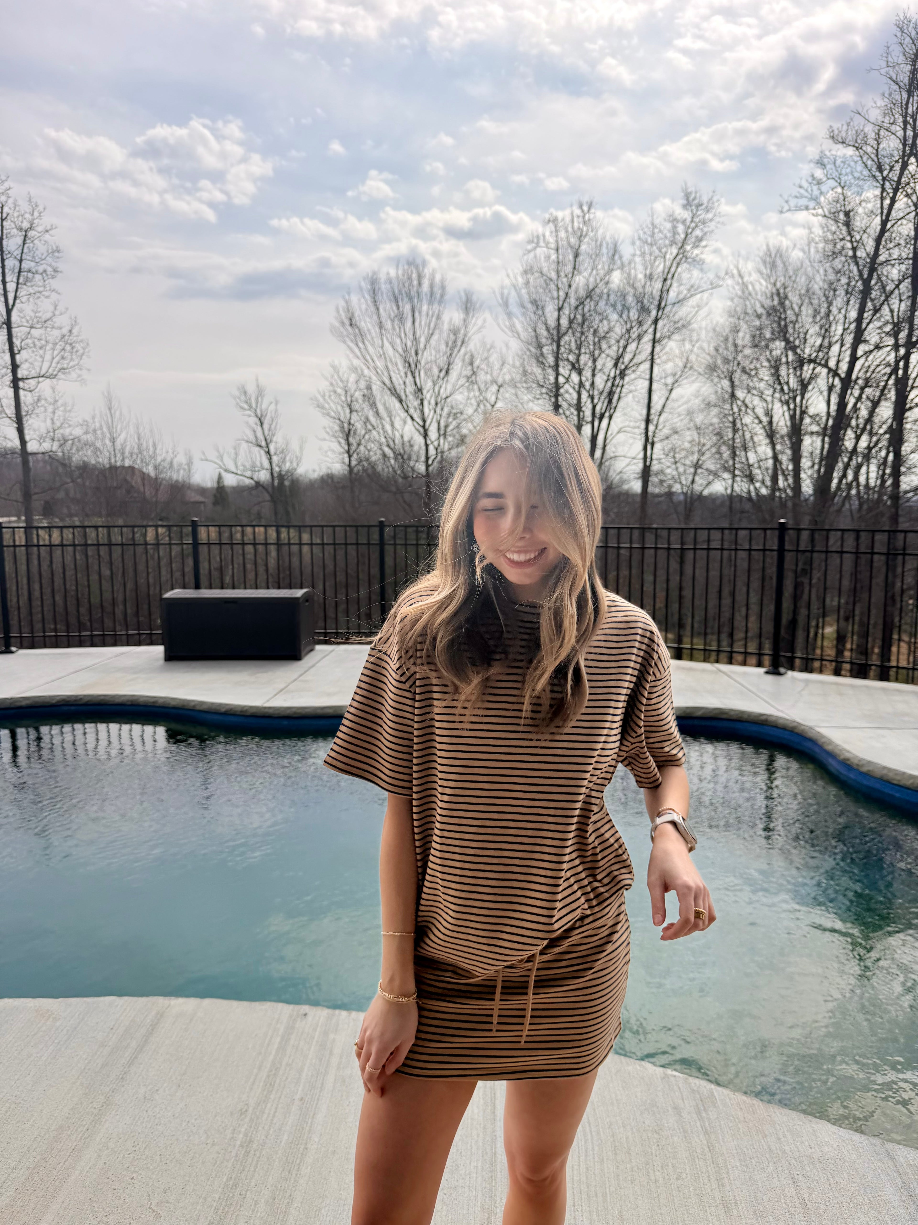 Woman standing by a pool wearing a brown dress with a striped set.