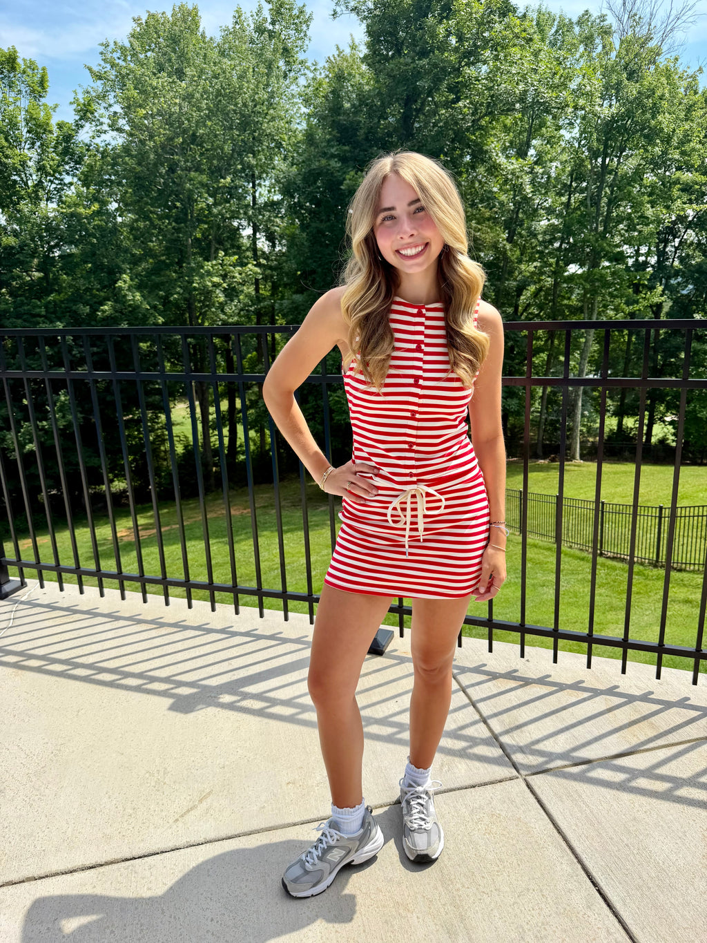 Woman in a red and white striped dress standing outdoors with trees in the background