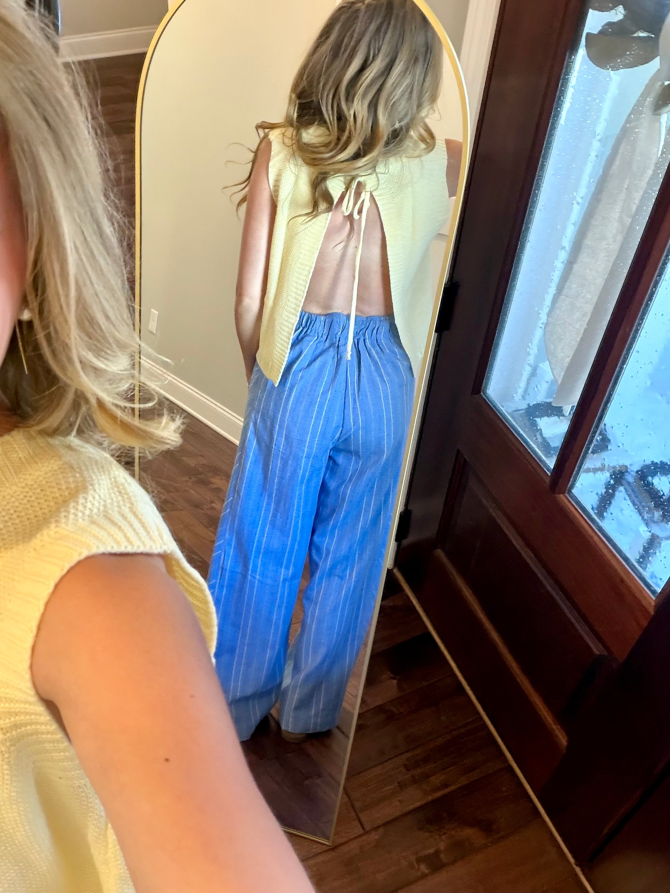 Woman wearing a yellow top and blue pants, standing in front of a mirror.