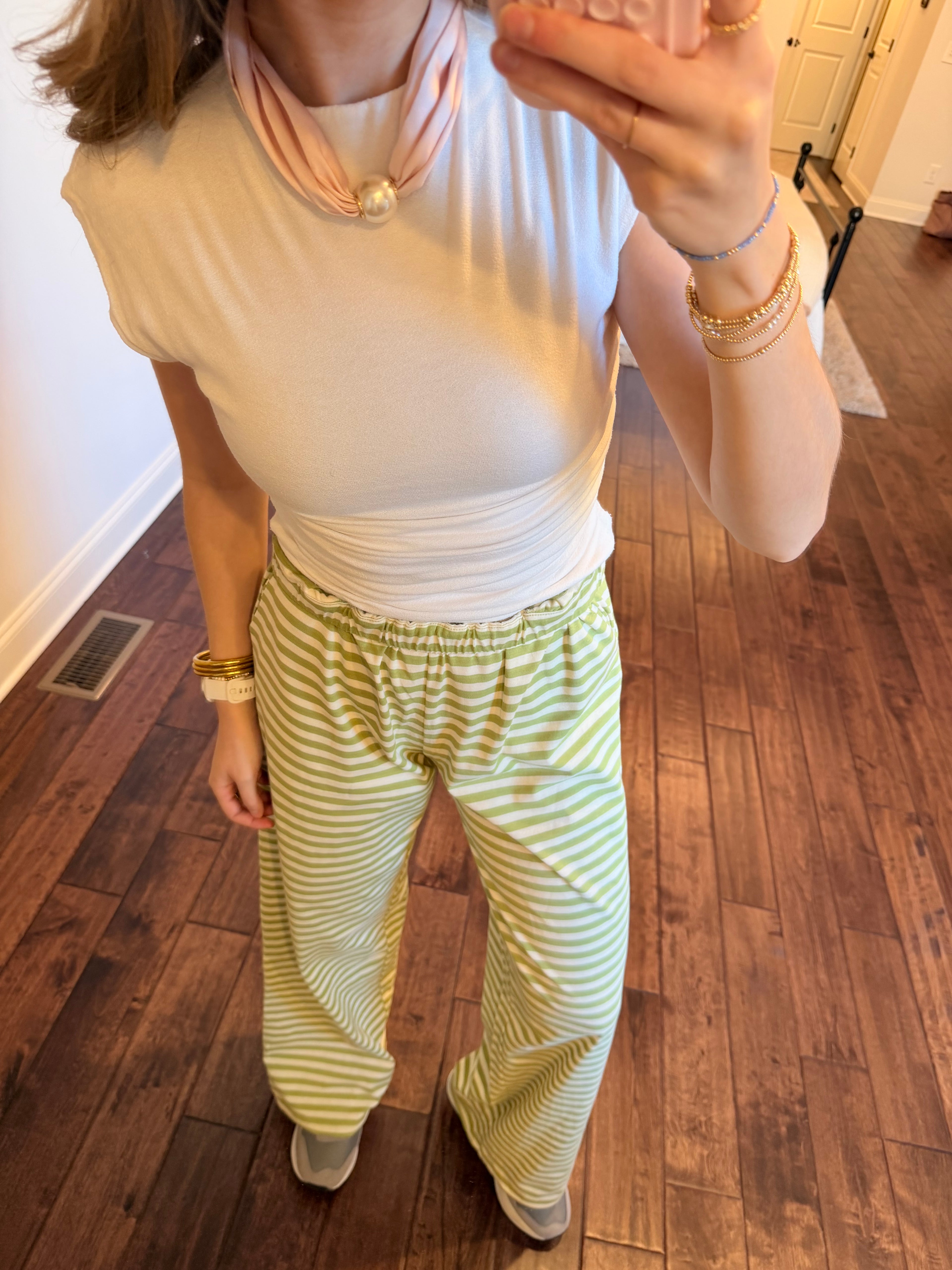 Person wearing a white top and green striped pants on a wooden floor.