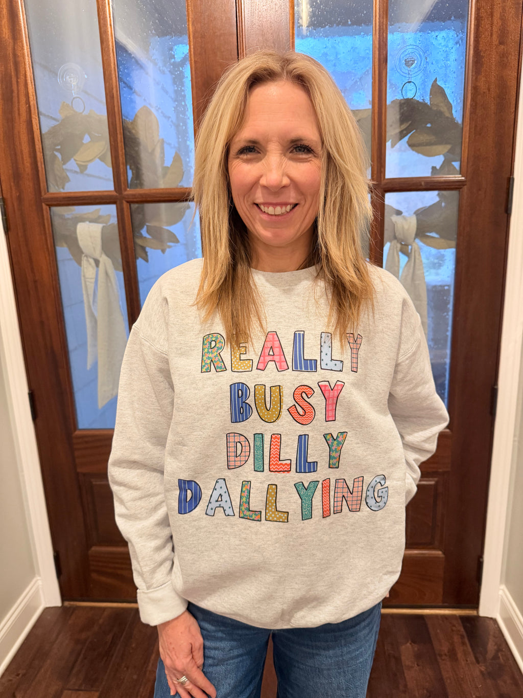 Person wearing a sweatshirt with colorful text in front of a wooden door.