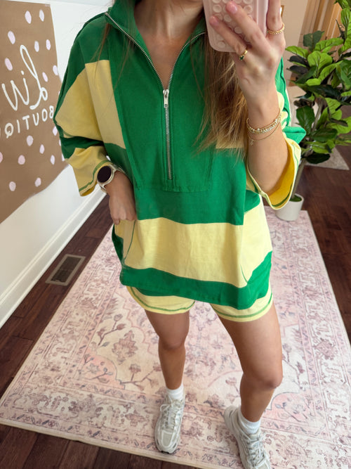 Person wearing a green and yellow outfit with a plant and patterned floor in the background