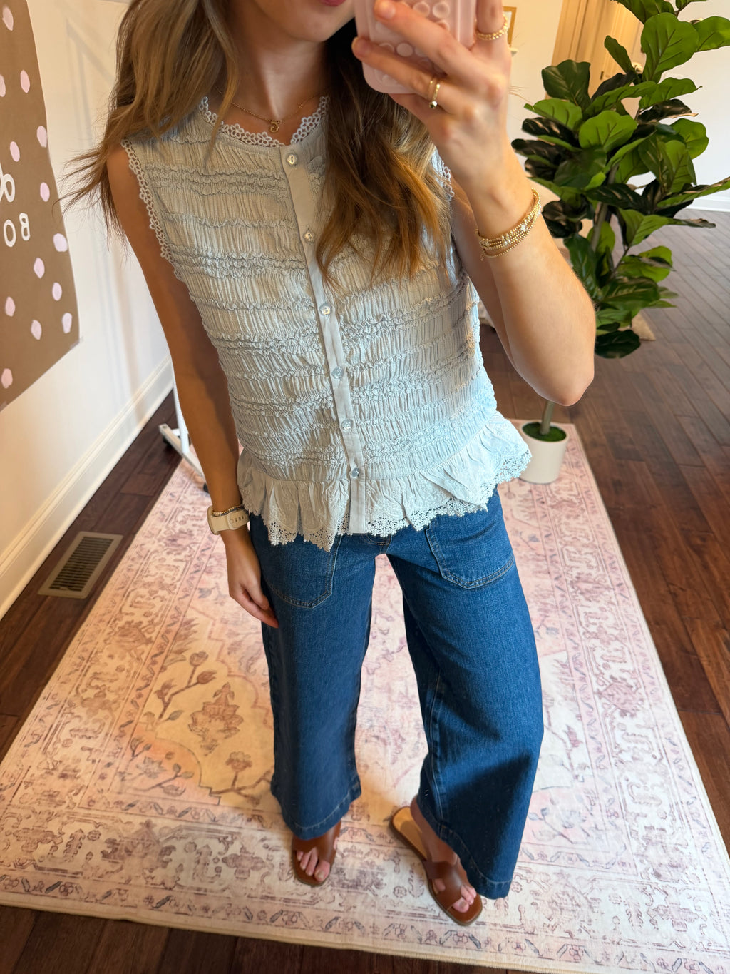 Person wearing a light blue textured top and blue jeans standing on a patterned rug.