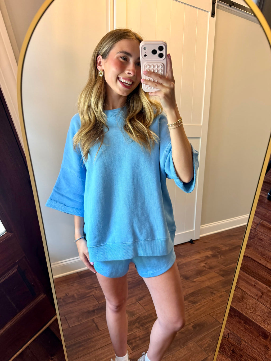 Woman taking a mirror selfie wearing a blue outfit in a room with wooden flooring.