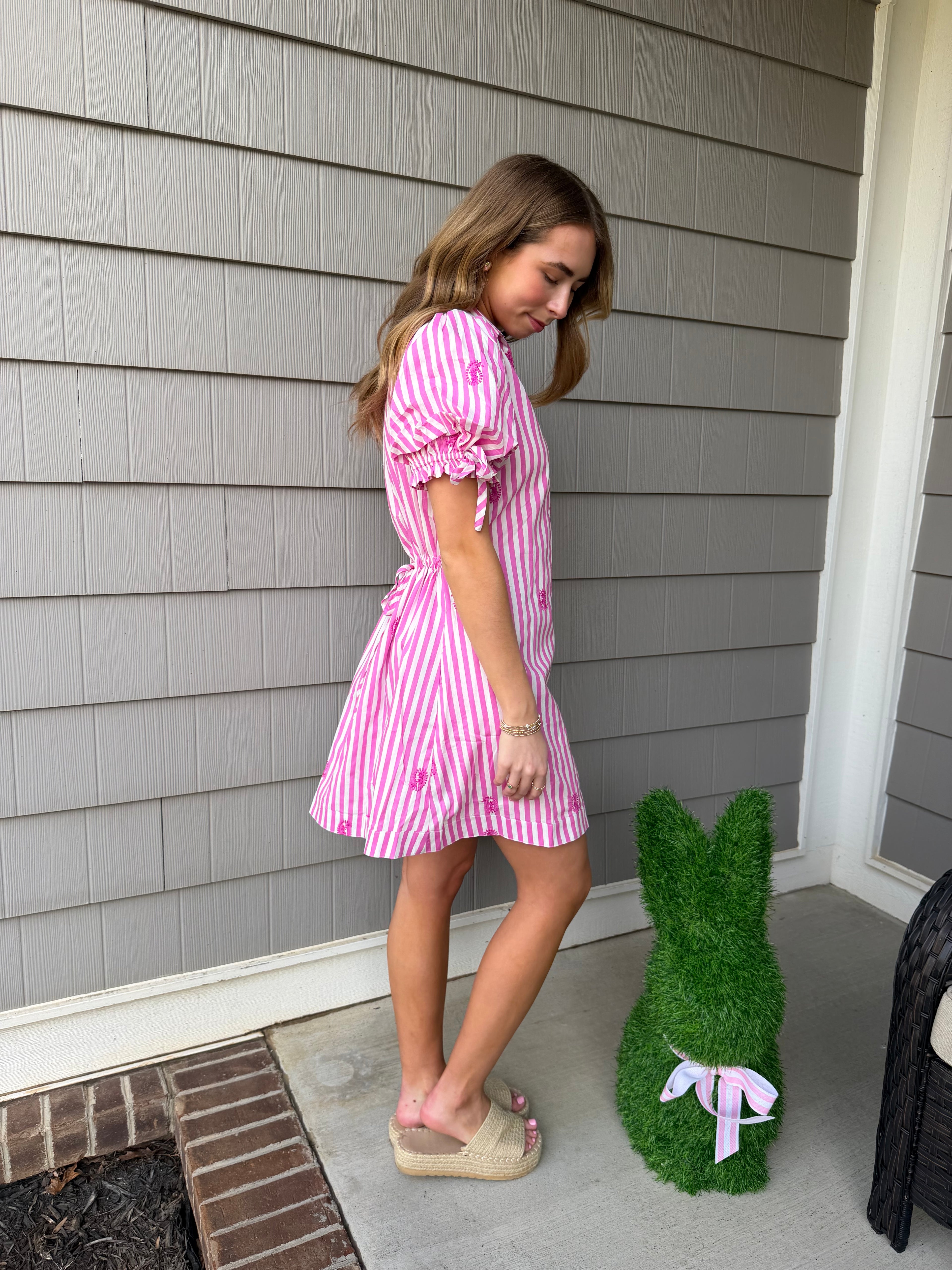 Person wearing a pink and white striped dress on a wooden deck.