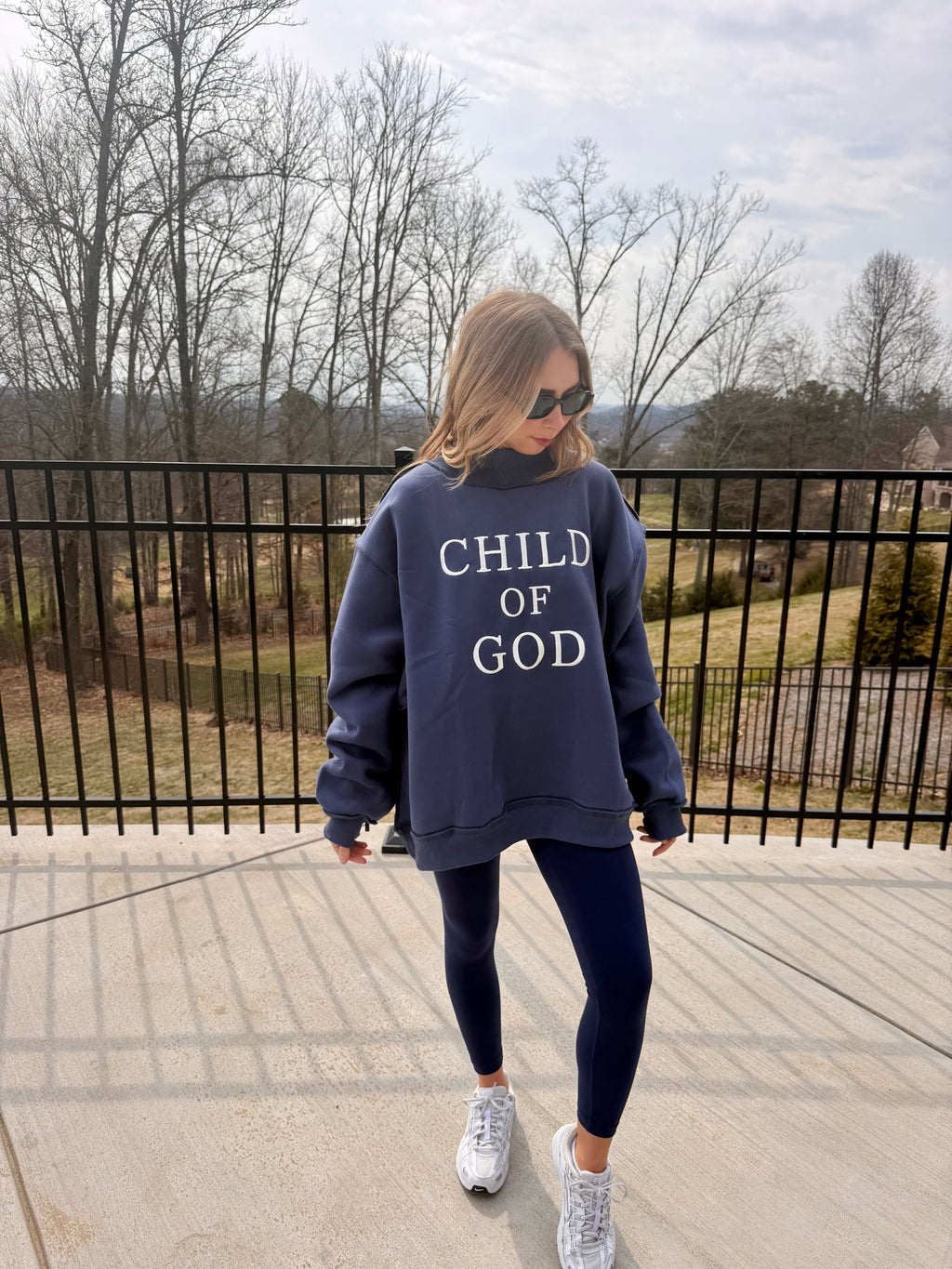 Person wearing a navy sweatshirt with 'CHILD OF GOD' text on a balcony.