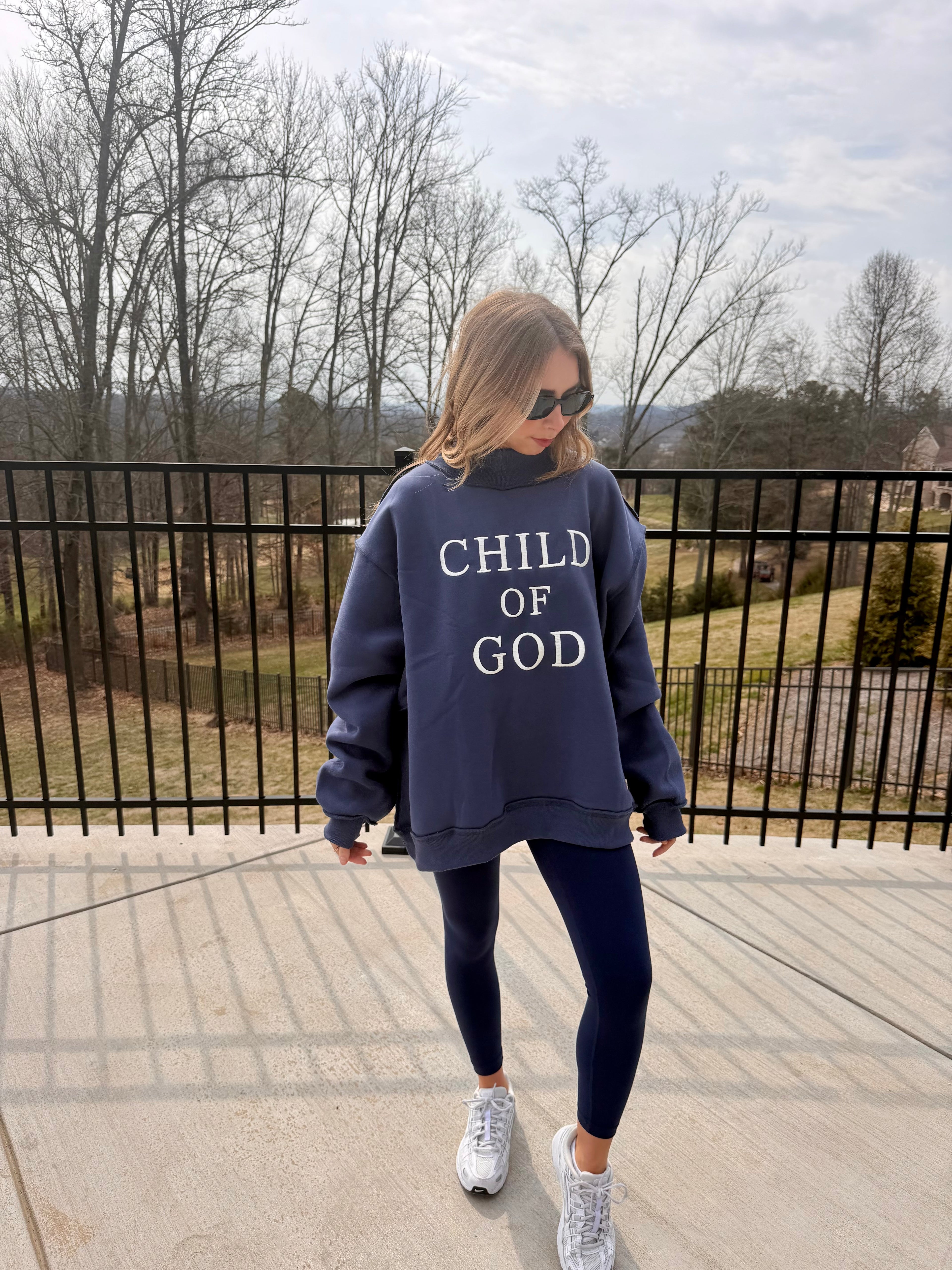 Person wearing a navy sweatshirt with 'CHILD OF GOD' text on a balcony.