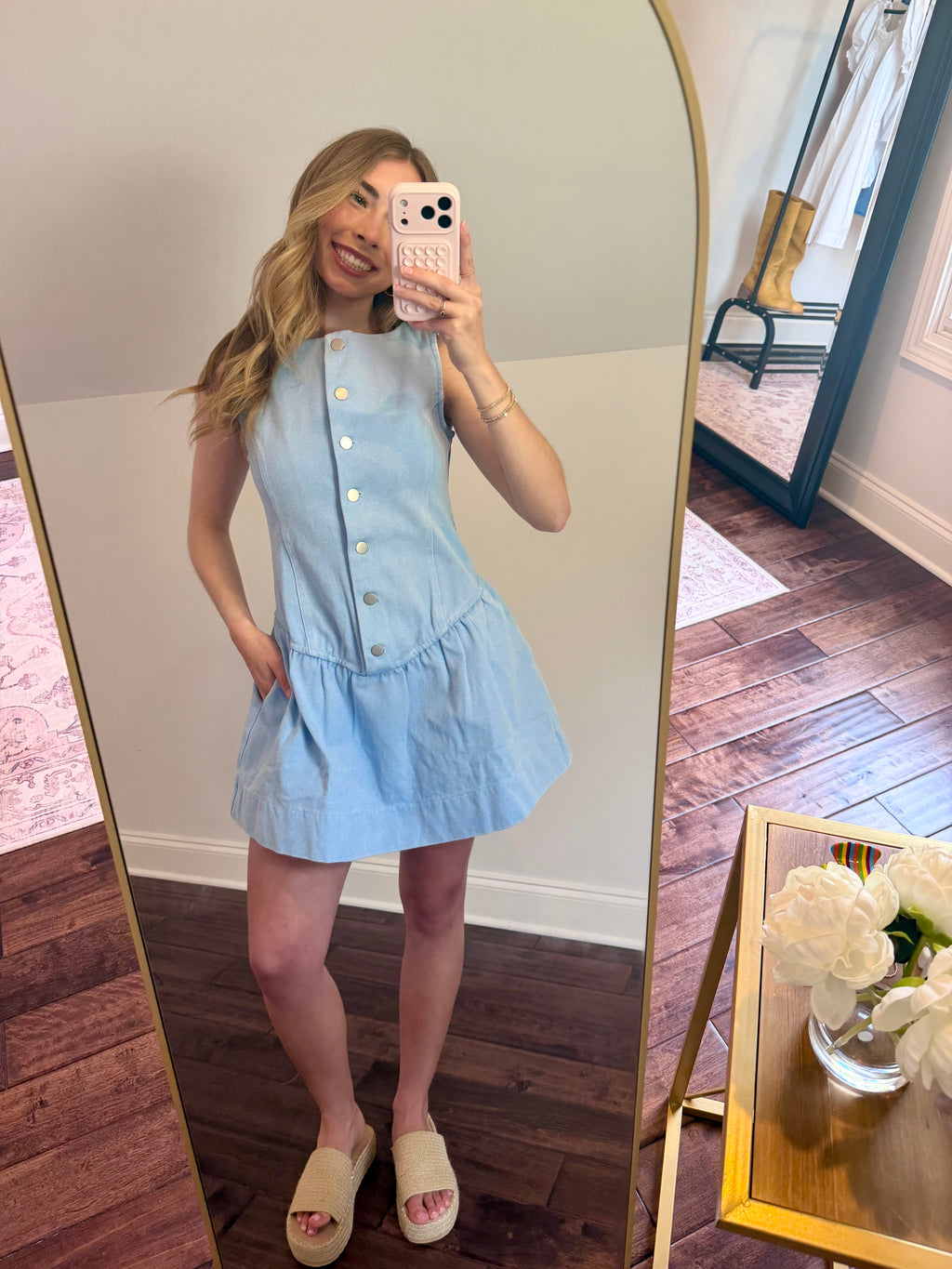 Woman taking a mirror selfie wearing a light blue dress in a room with wooden flooring.