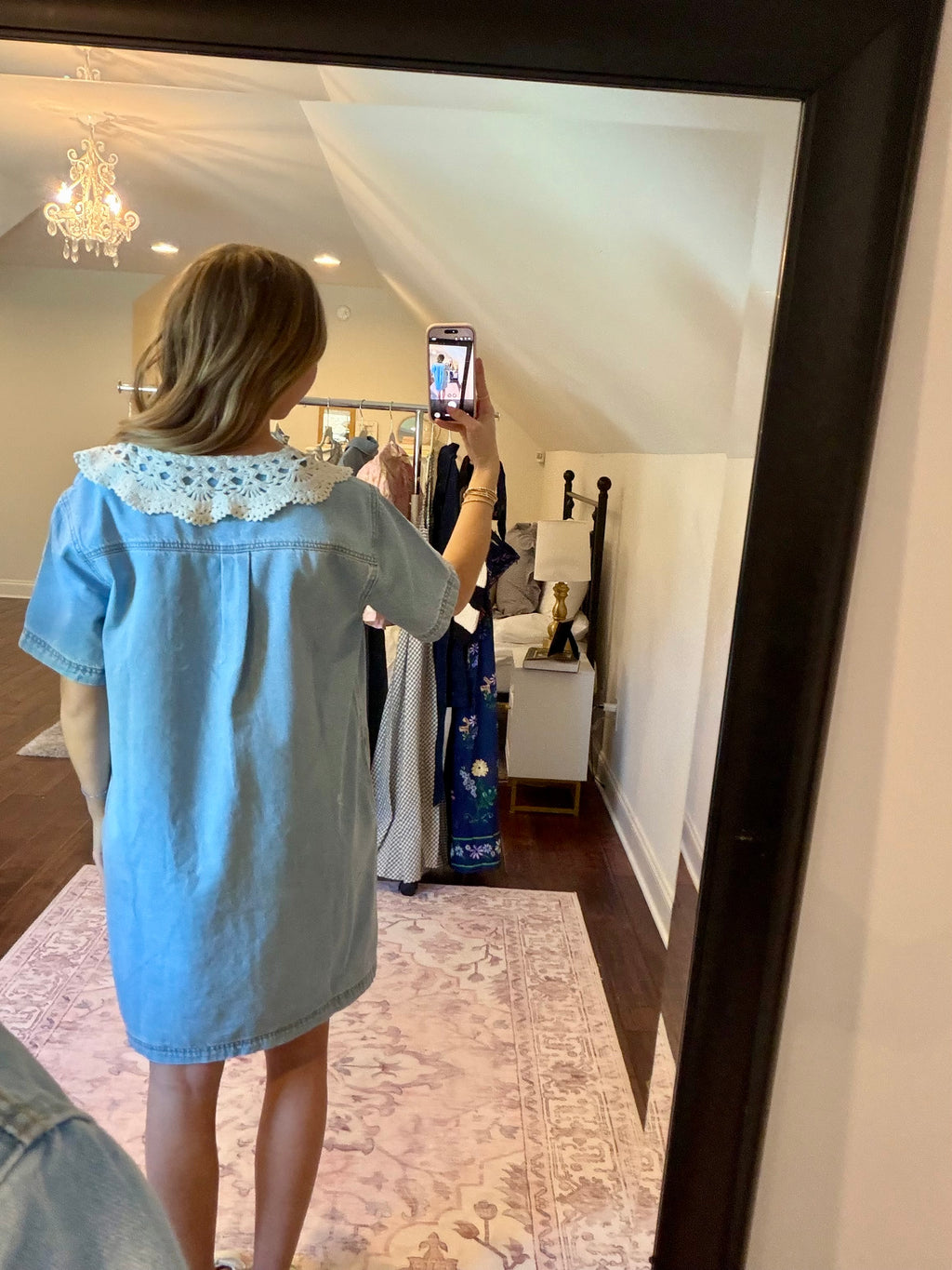 Woman taking a mirror selfie wearing a light blue dress in a home setting.