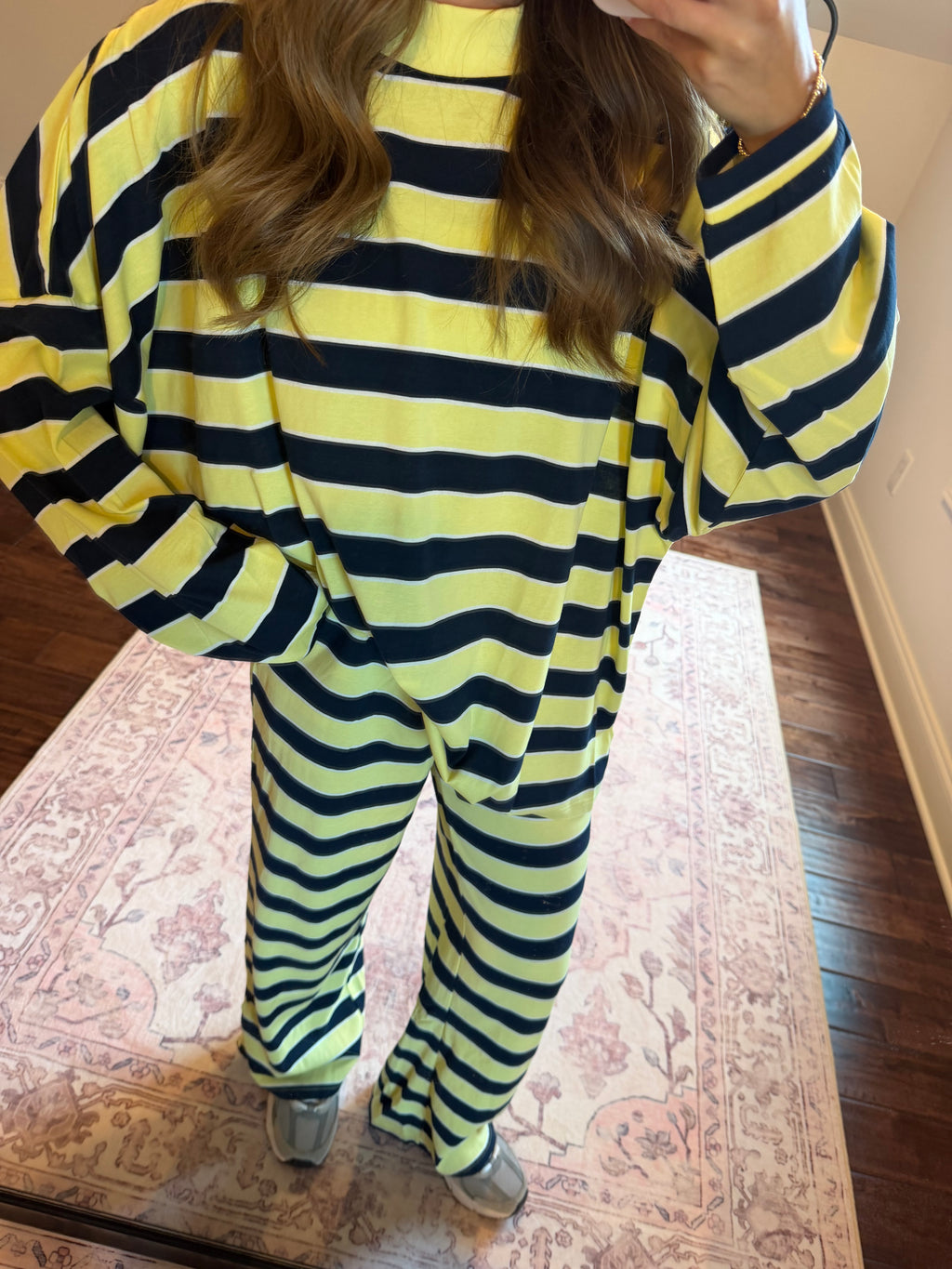 A person wearing a matching two-piece loungewear set with bold horizontal lime green and black stripes, standing on a patterned rug in a home setting.