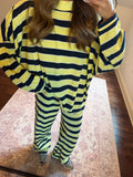 A person wearing a matching two-piece loungewear set with bold horizontal lime green and black stripes, standing on a patterned rug in a home setting.