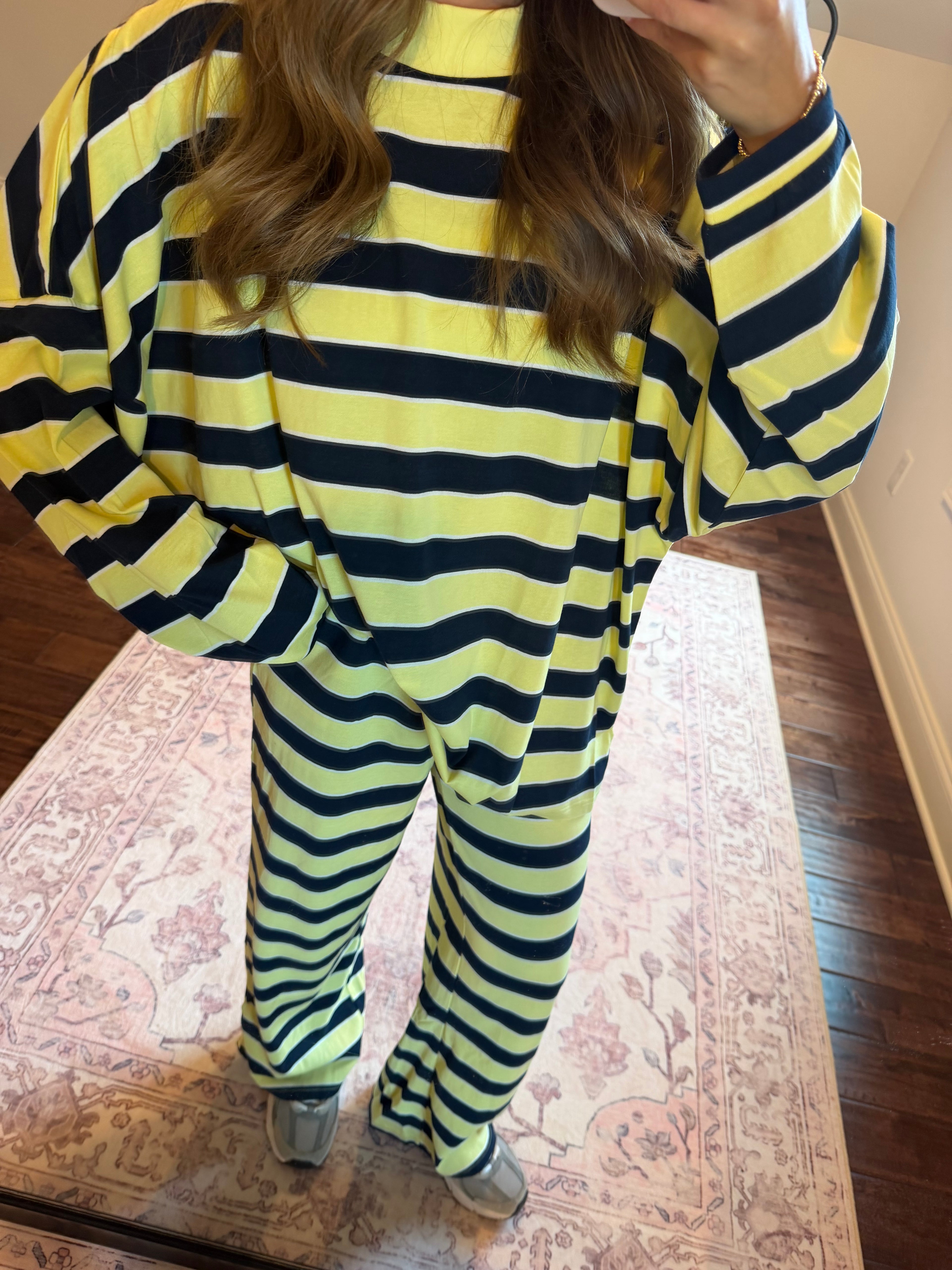 A person wearing a matching two-piece loungewear set with bold horizontal lime green and black stripes, standing on a patterned rug in a home setting.