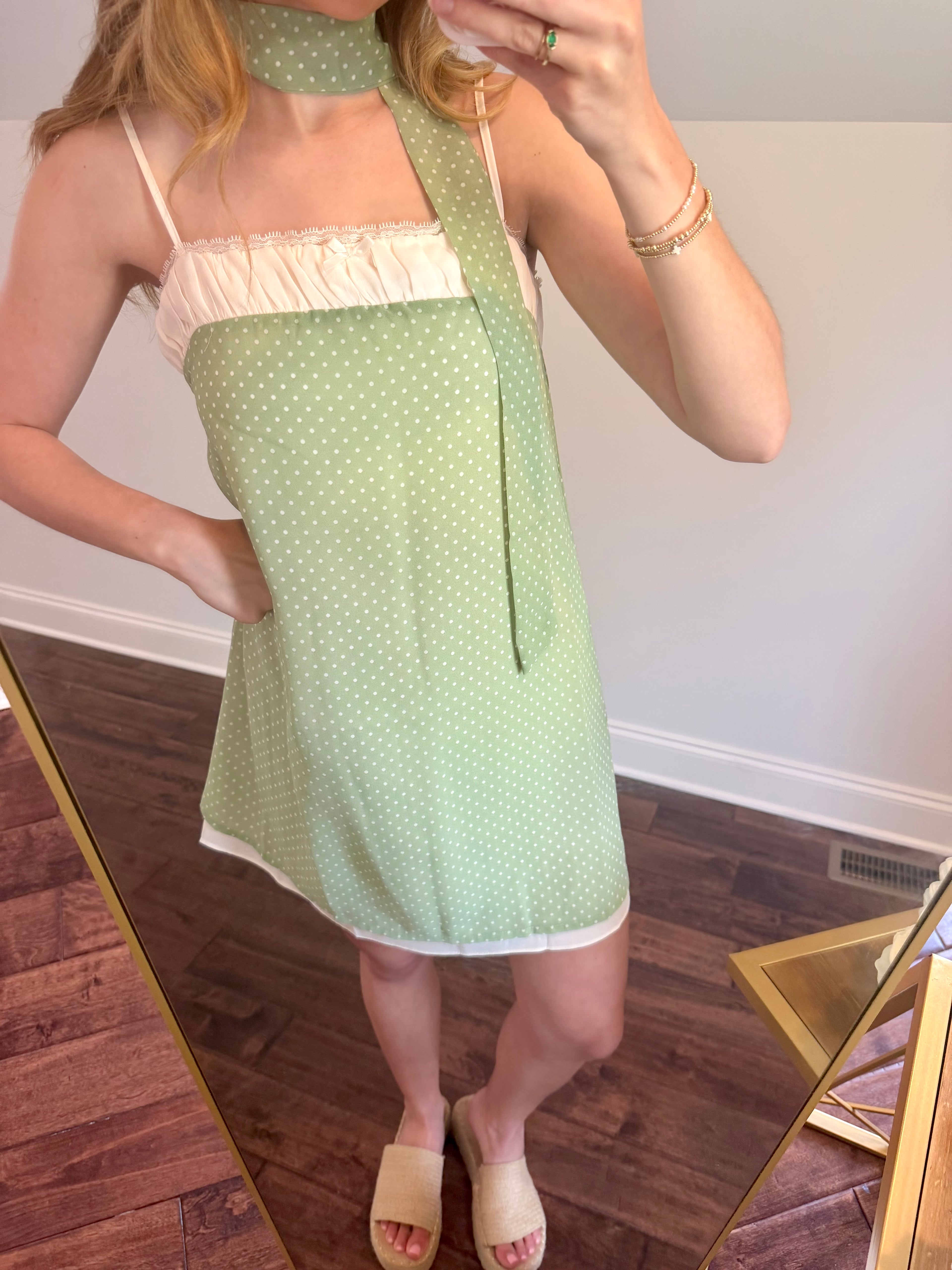 Person wearing a green polka dot dress with a white top, standing in front of a mirror.