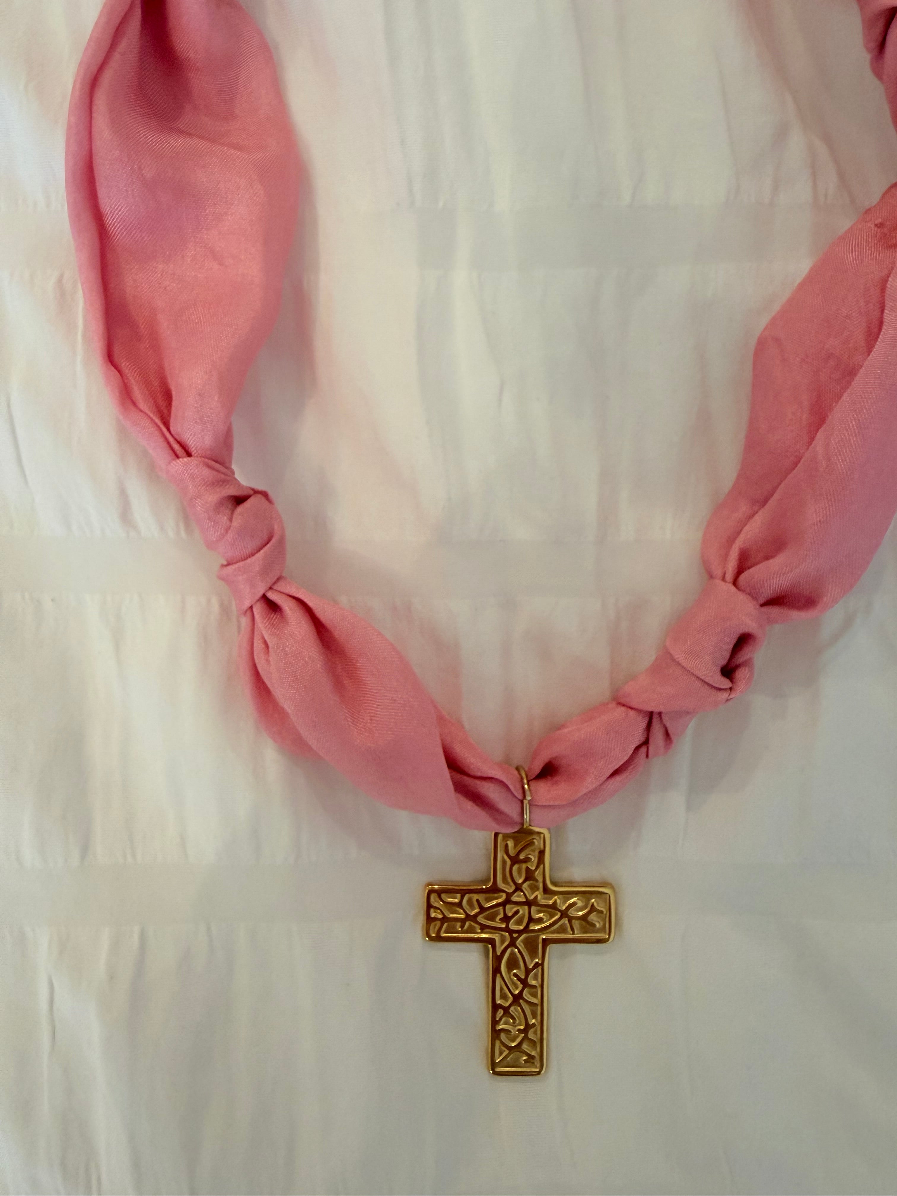 Pink scarf necklace with a gold cross on a white background