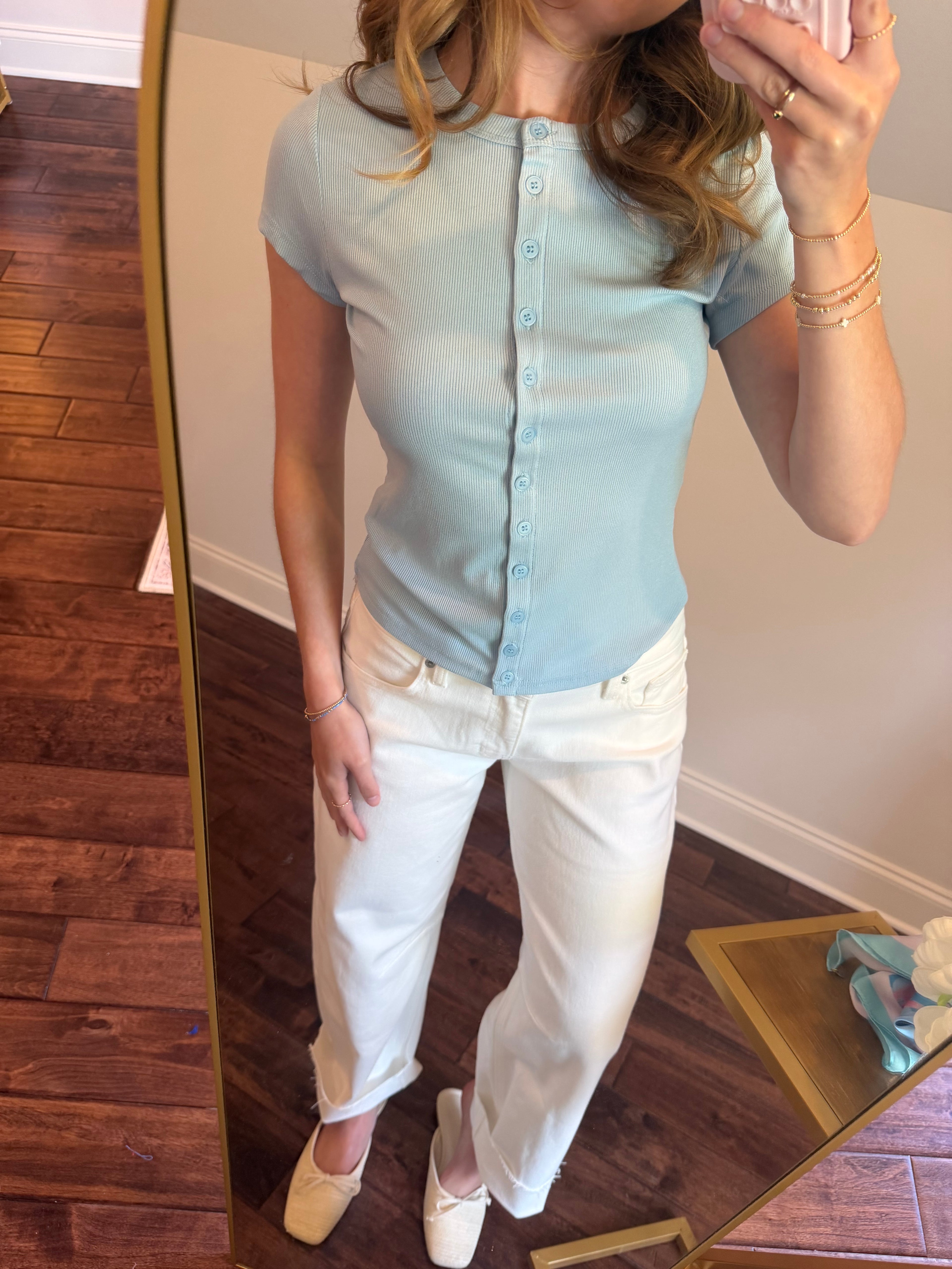Person wearing a light blue button-up shirt and white pants, standing in front of a mirror.