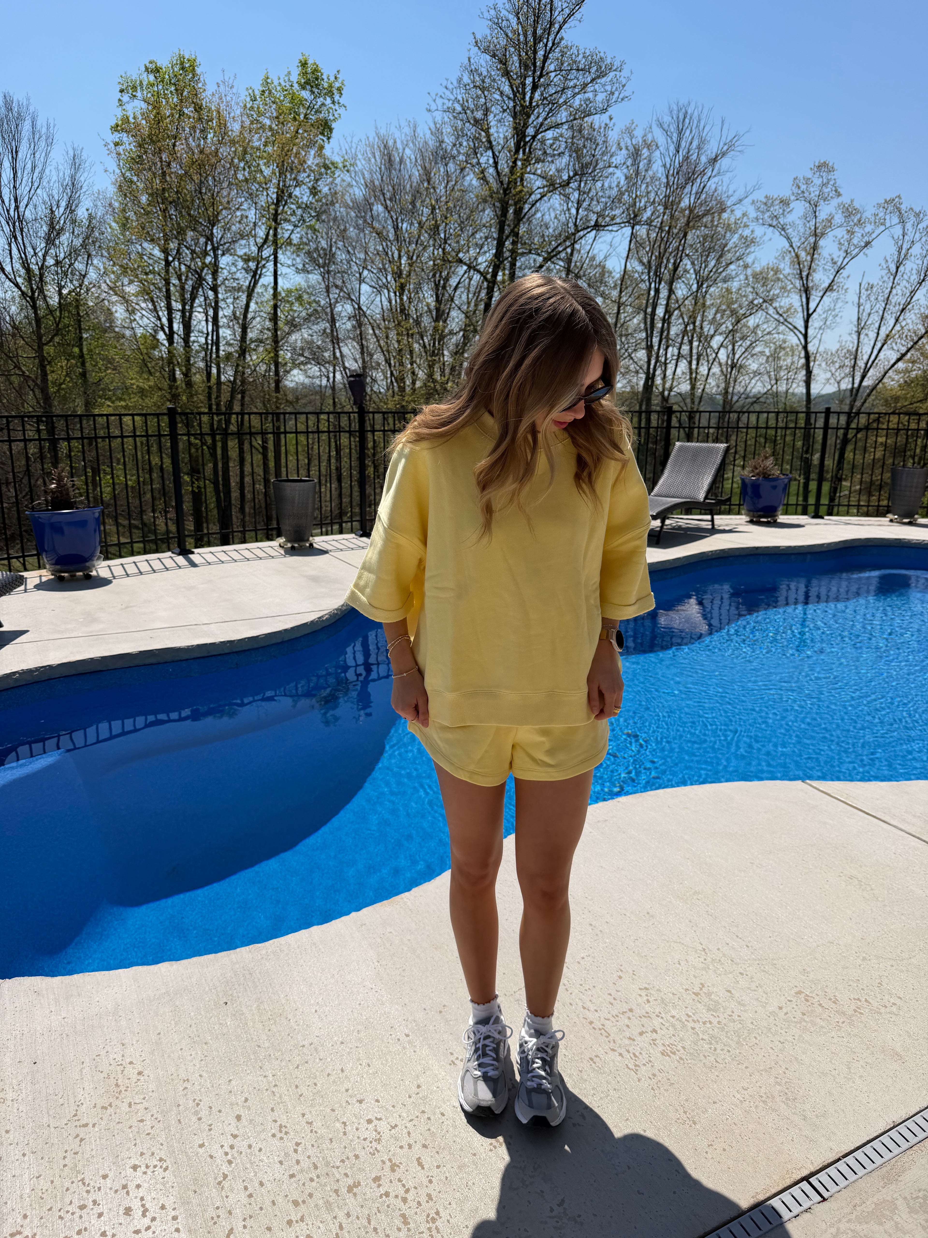 Person in a yellow shirt standing by a pool on a sunny day