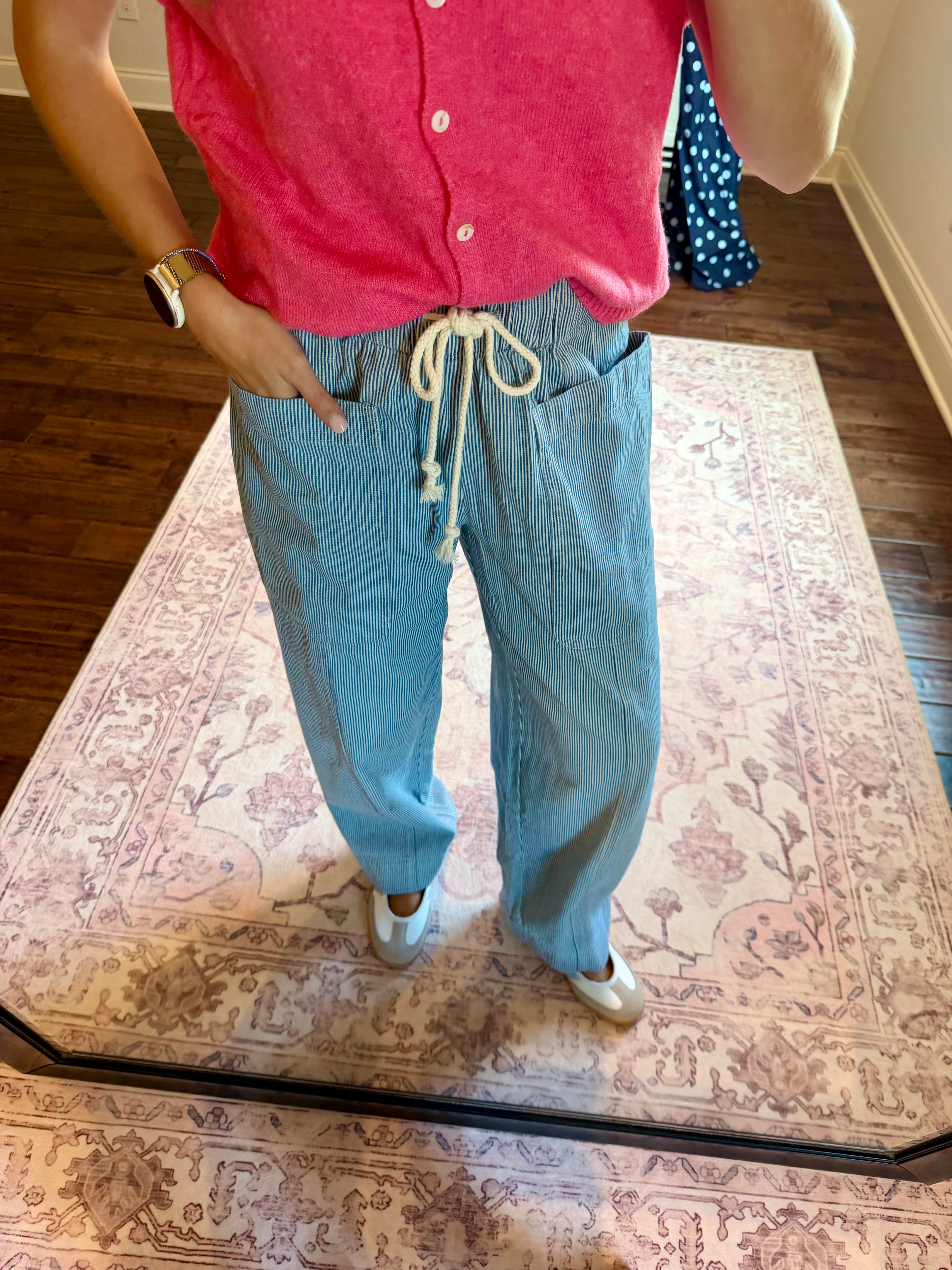 A person wearing light blue wide-leg drawstring pants and a pink top, standing on a patterned rug in a home setting.