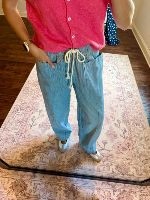 A person wearing light blue wide-leg drawstring pants and a pink top, standing on a patterned rug in a home setting.