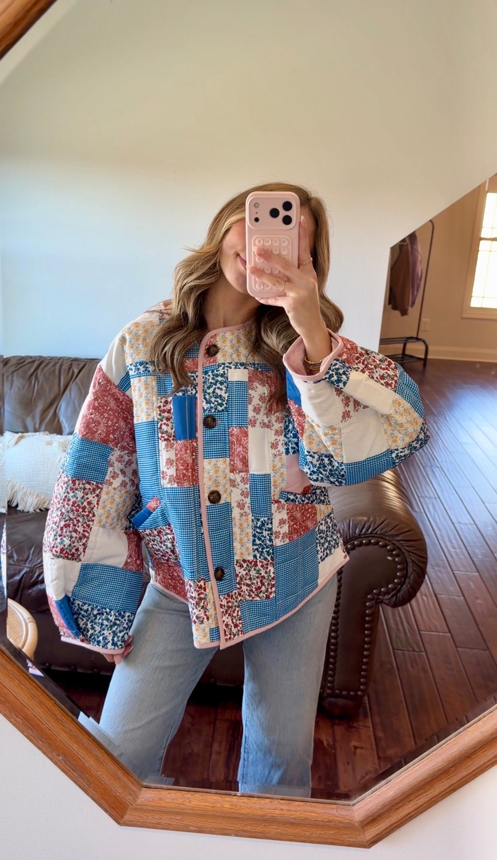 Person wearing a patchwork jacket taking a mirror selfie in a living room.
