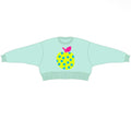 A light mint green long-sleeve crewneck sweater featuring a stylized yellow pineapple graphic on the chest with blue polka dots and a pink leaf.