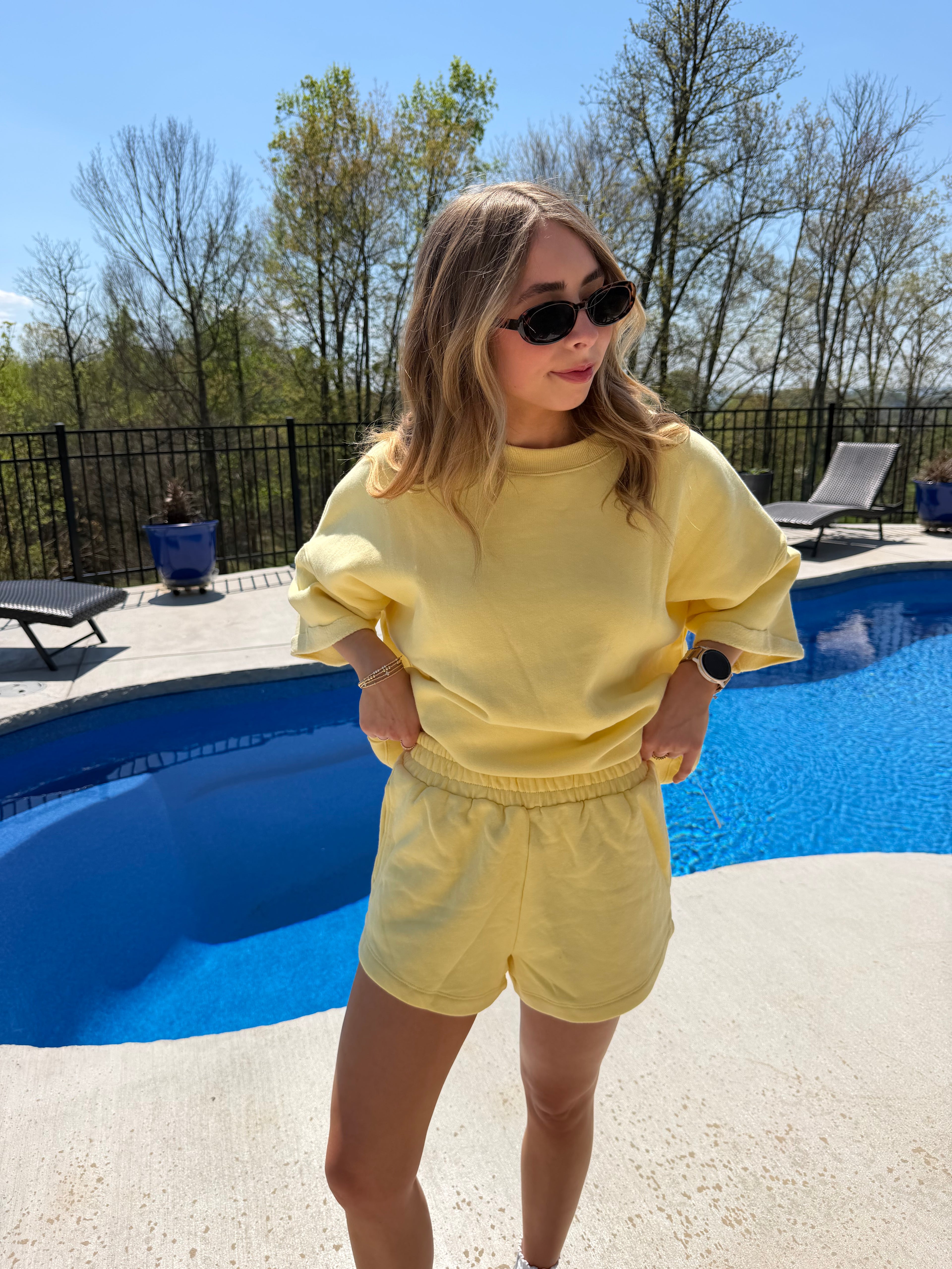 Woman in a yellow outfit standing by a pool on a clear day