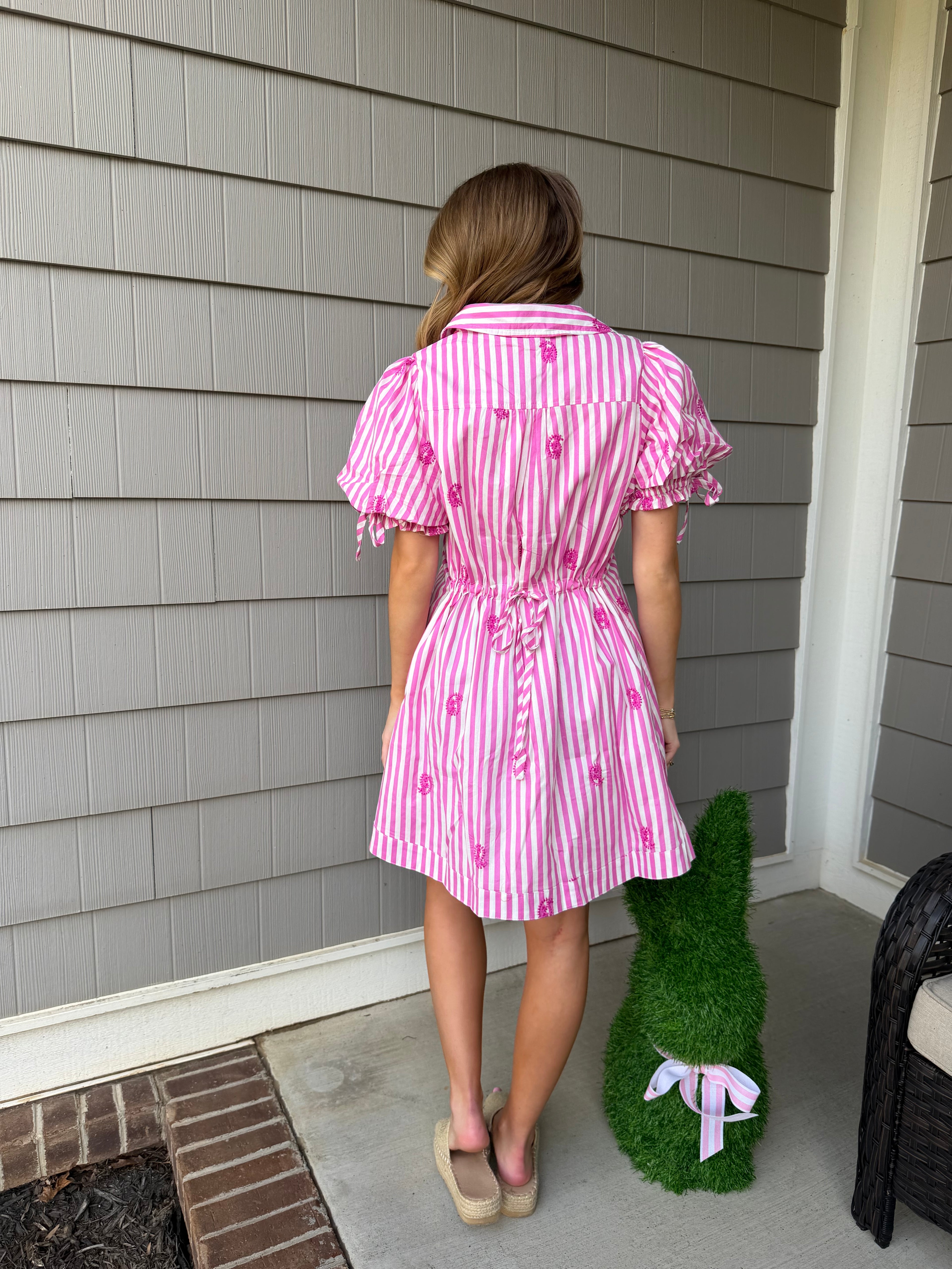 Woman wearing a pink and white striped dress on a wooden deck.