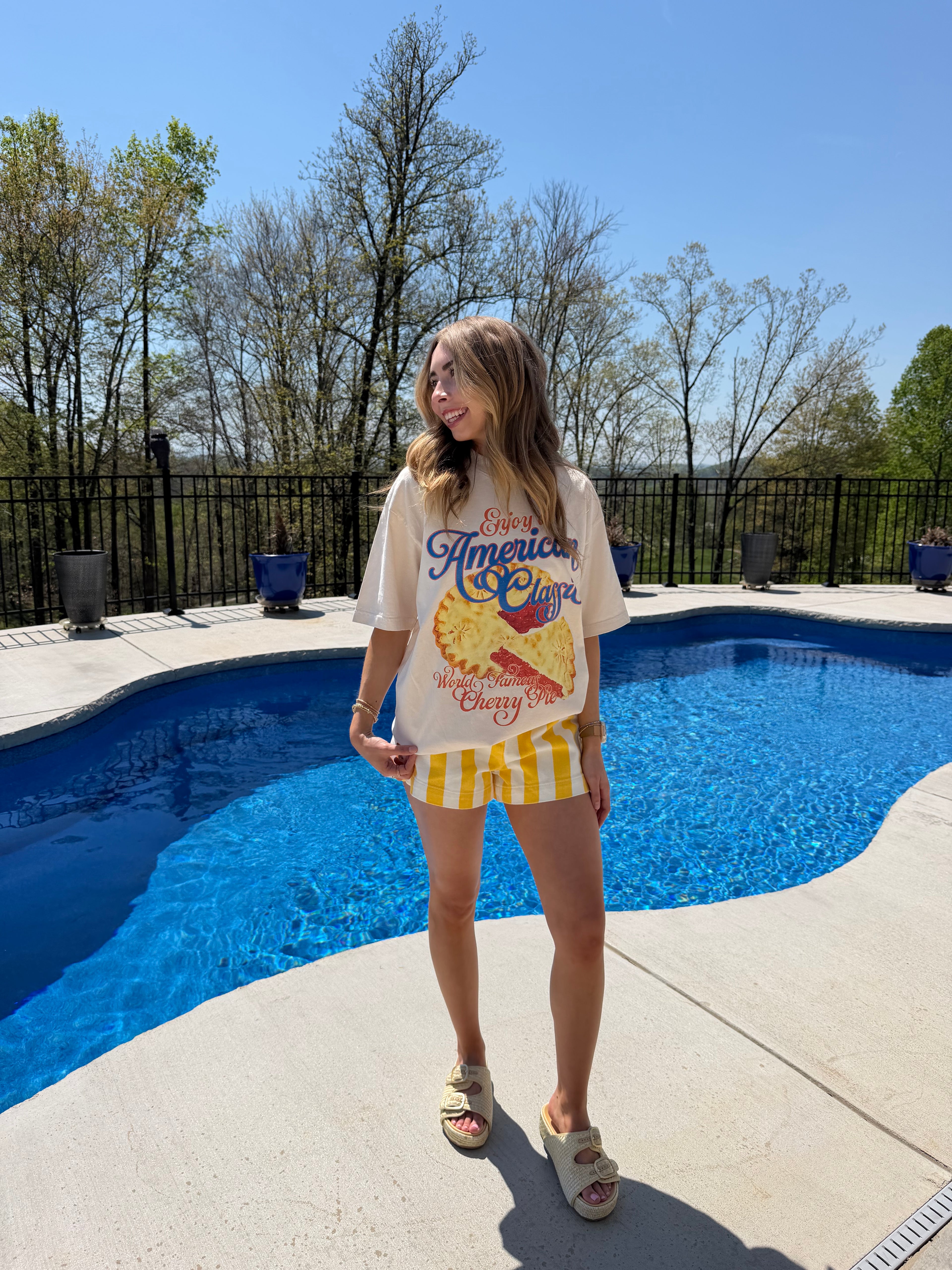 Person holding a colorful bag by a poolside with trees and clear sky in the background