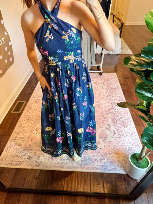Woman taking a mirror selfie wearing a blue floral dress  in a room with a plant and decorative wall art.