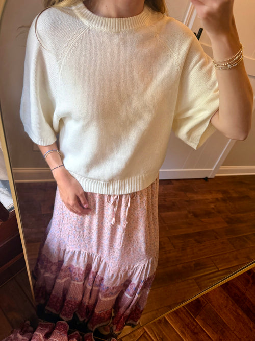 Person wearing a white sweater and patterned skirt in front of a mirror.
