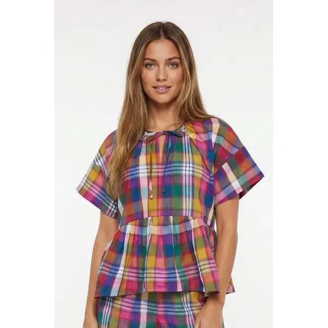 A woman modeling a short-sleeve plaid top with a tie neckline and a matching pleated peplum waist, shown against a plain light gray studio background.