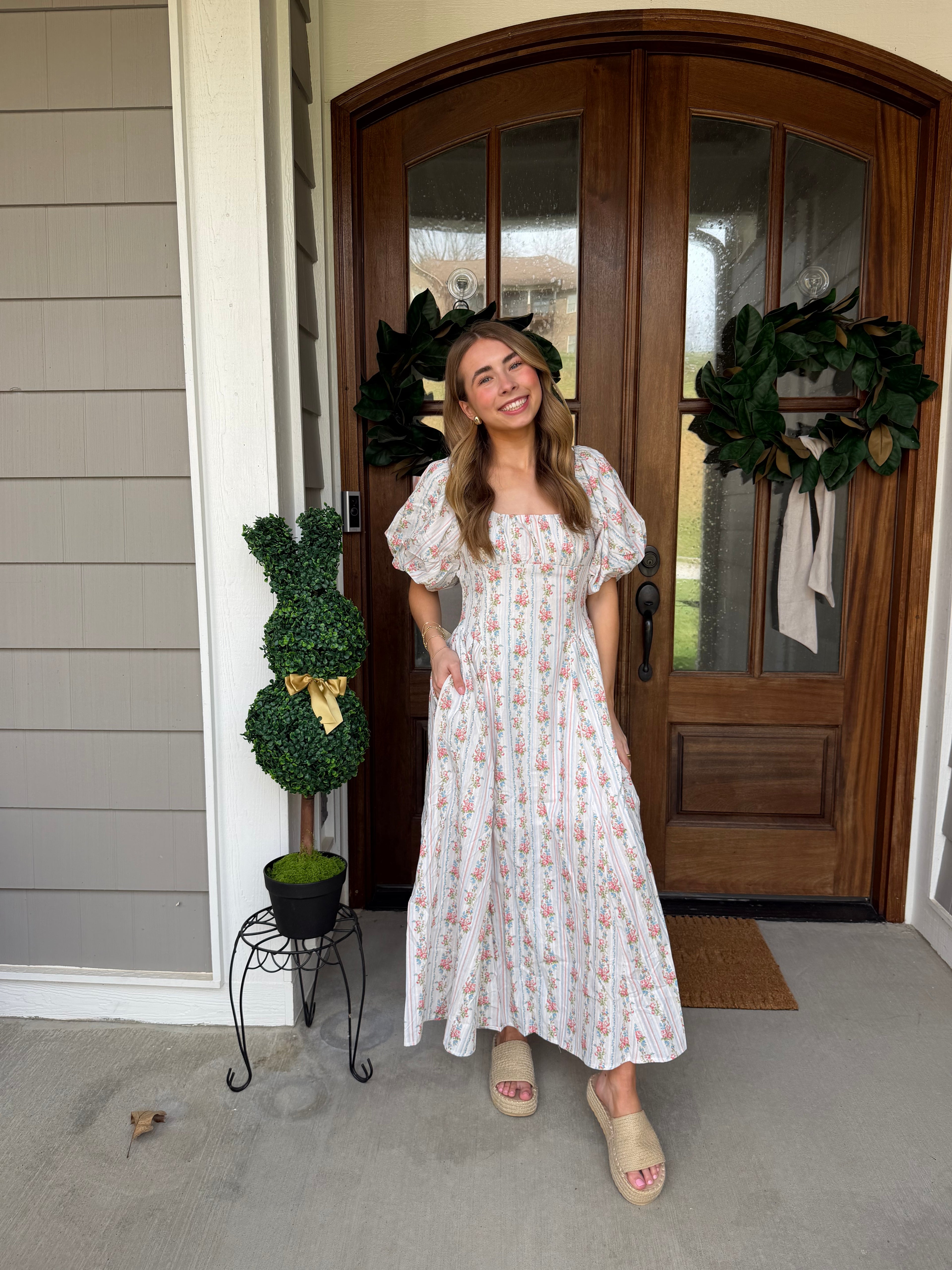 Woman in a white dress standing in front of a wooden door with wreaths.