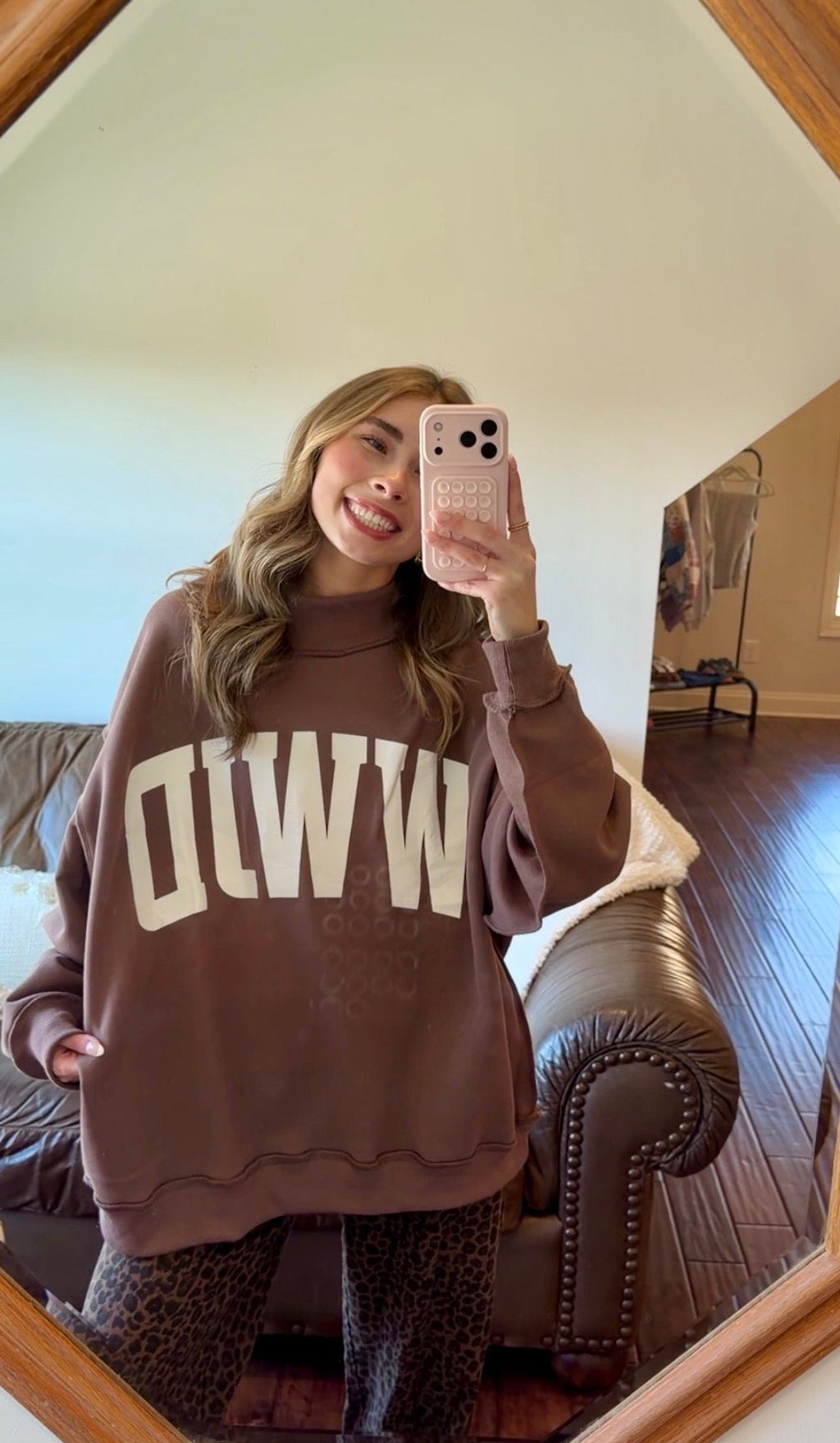 Person wearing a brown sweater with 'WWJD' text, standing in a room with a mirror.