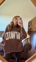 Person wearing a brown sweater with 'WWJD' text, standing in a room with a mirror.
