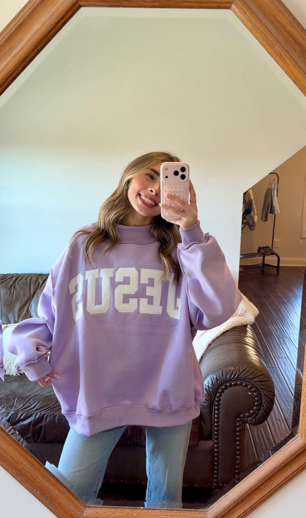 Person wearing a purple sweatshirt with 'Jesus' printed on it, taking a mirror selfie.