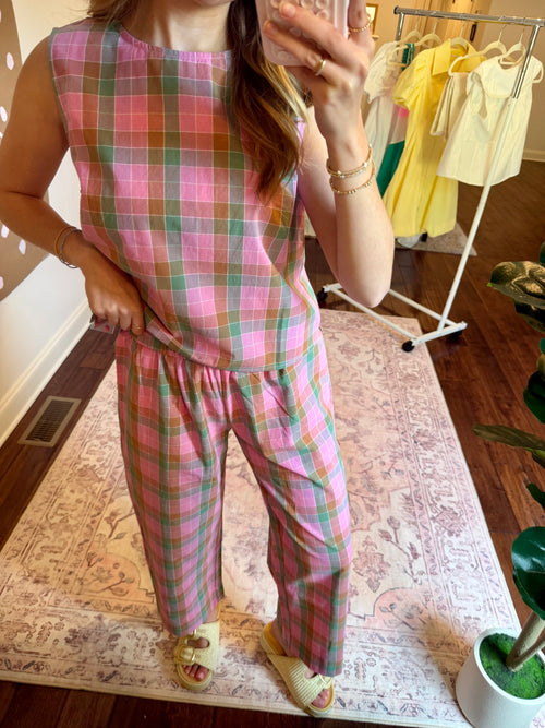 Person wearing a pink plaid outfit taking a mirror selfie in a room with a clothing rack in the background.