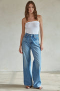Woman wearing a white strapless top and blue jeans against a plain background