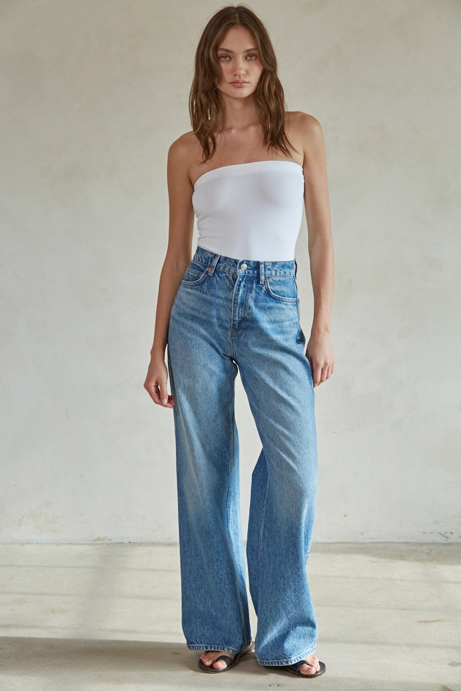 Woman wearing a white strapless top and blue jeans against a plain background