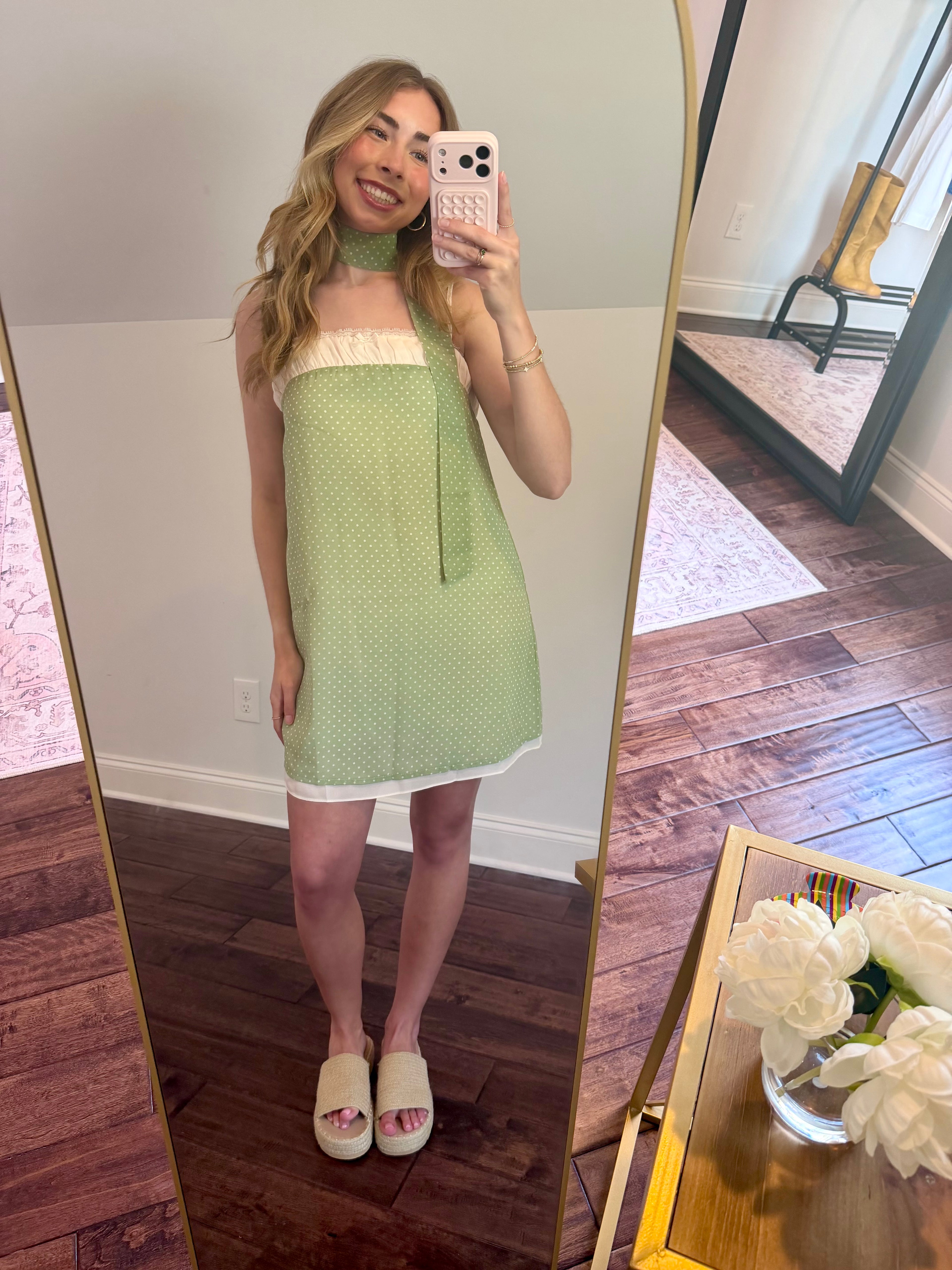 Woman taking a mirror selfie wearing a green dress in a room with wooden flooring.