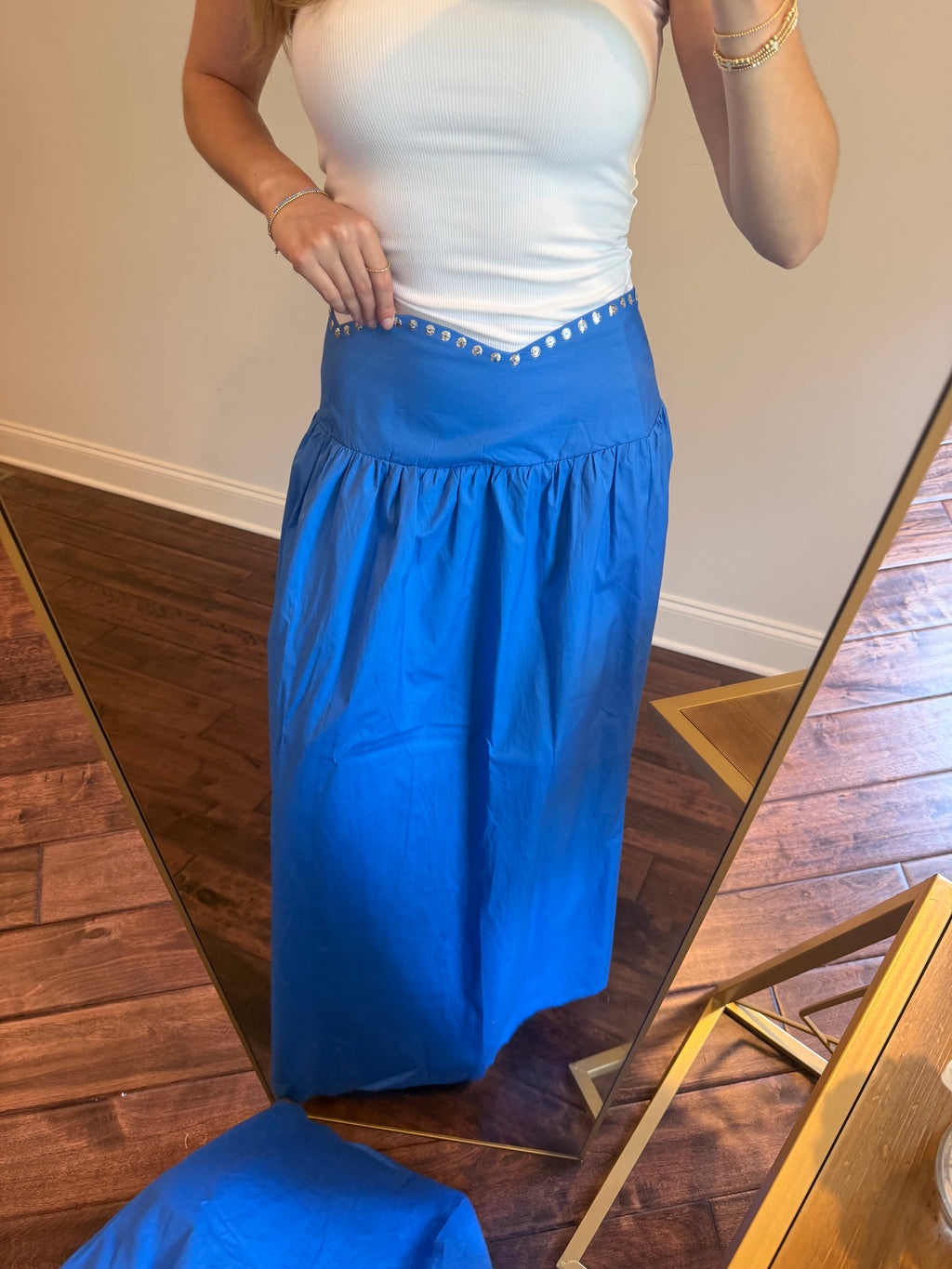 Person wearing a blue skirt and white top in front of a mirror.