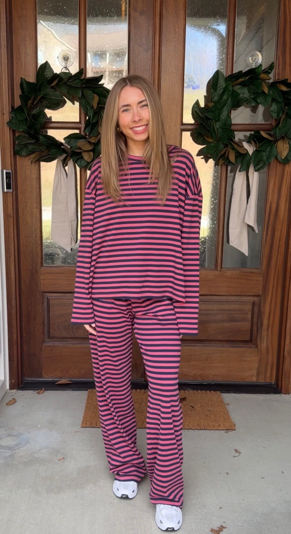 Person wearing a pink and purple striped outfit standing in front of a wooden door with wreaths.