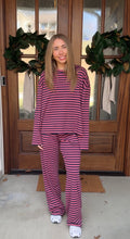 Person wearing a pink and purple striped outfit standing in front of a wooden door with wreaths.