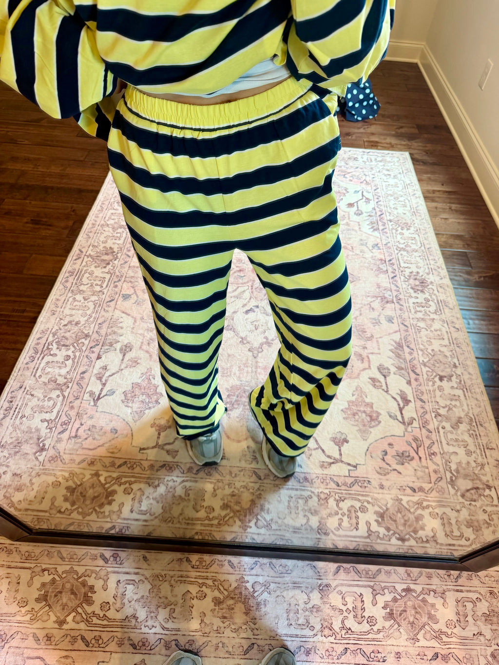 A person wearing a matching neon yellow and black striped sweatshirt and sweatpants set, standing on a patterned area rug in a home setting.