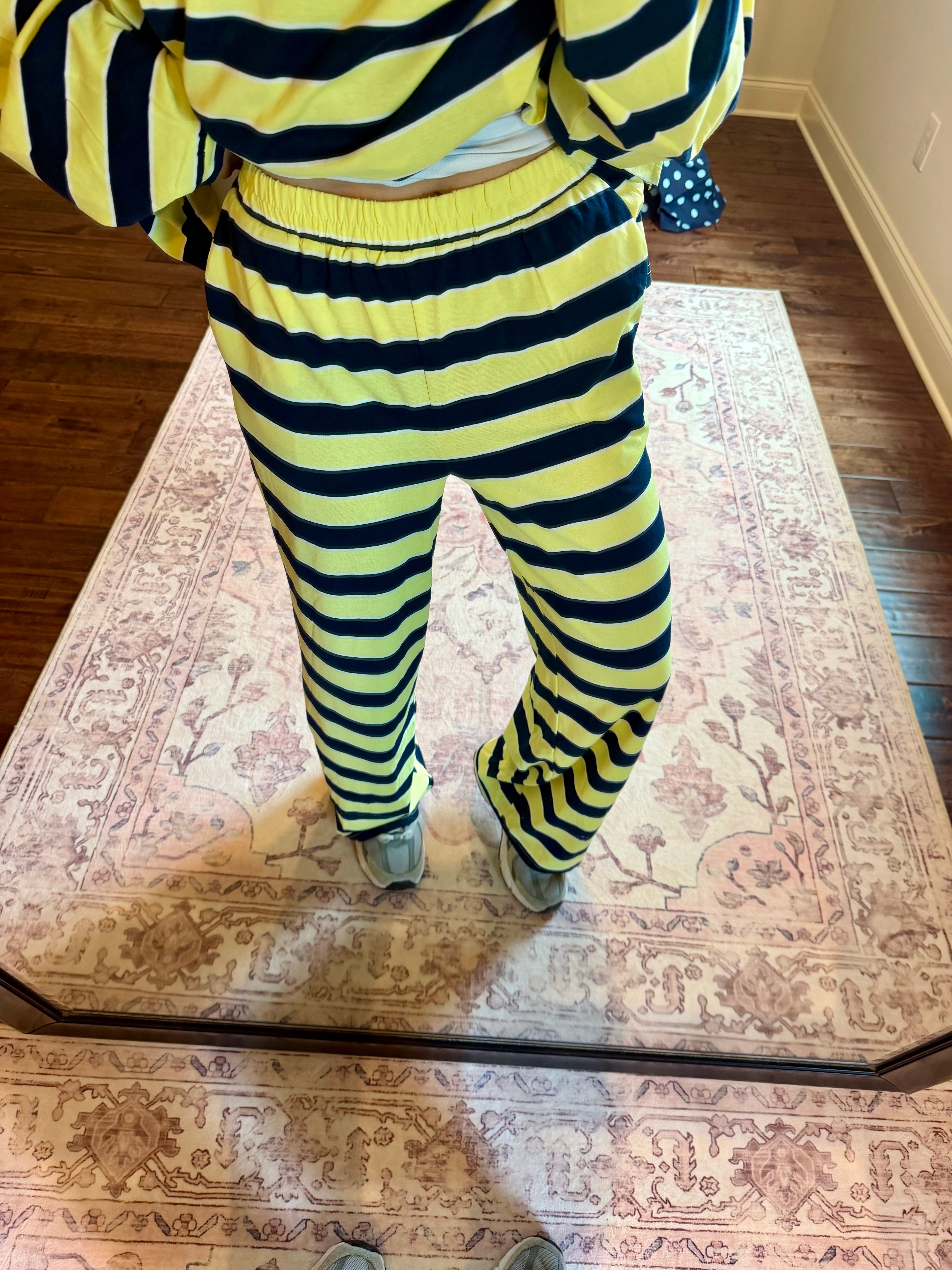 A person wearing a matching neon yellow and black striped sweatshirt and sweatpants set, standing on a patterned area rug in a home setting.