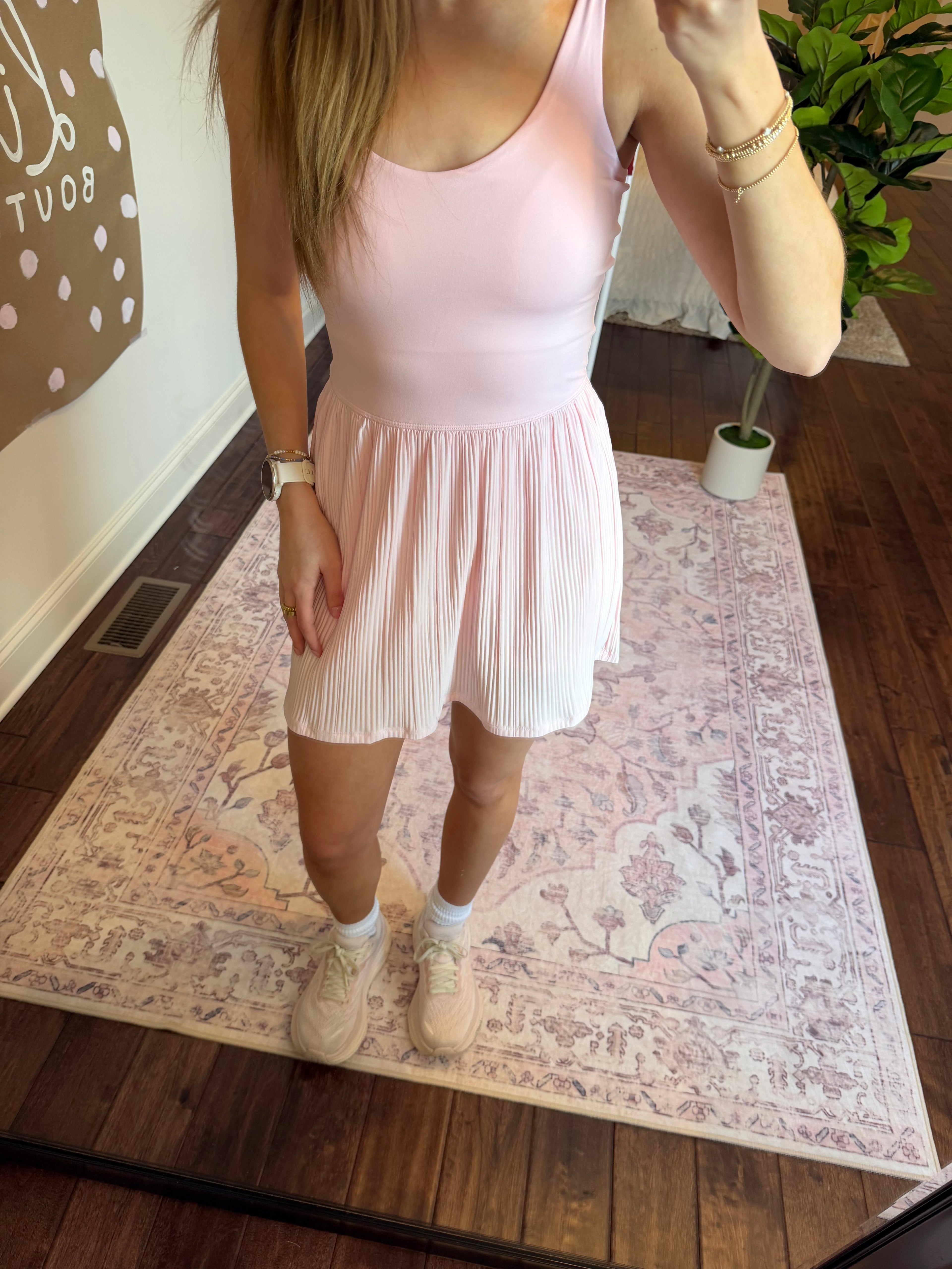 Person wearing a pink active dress standing on a patterned rug.