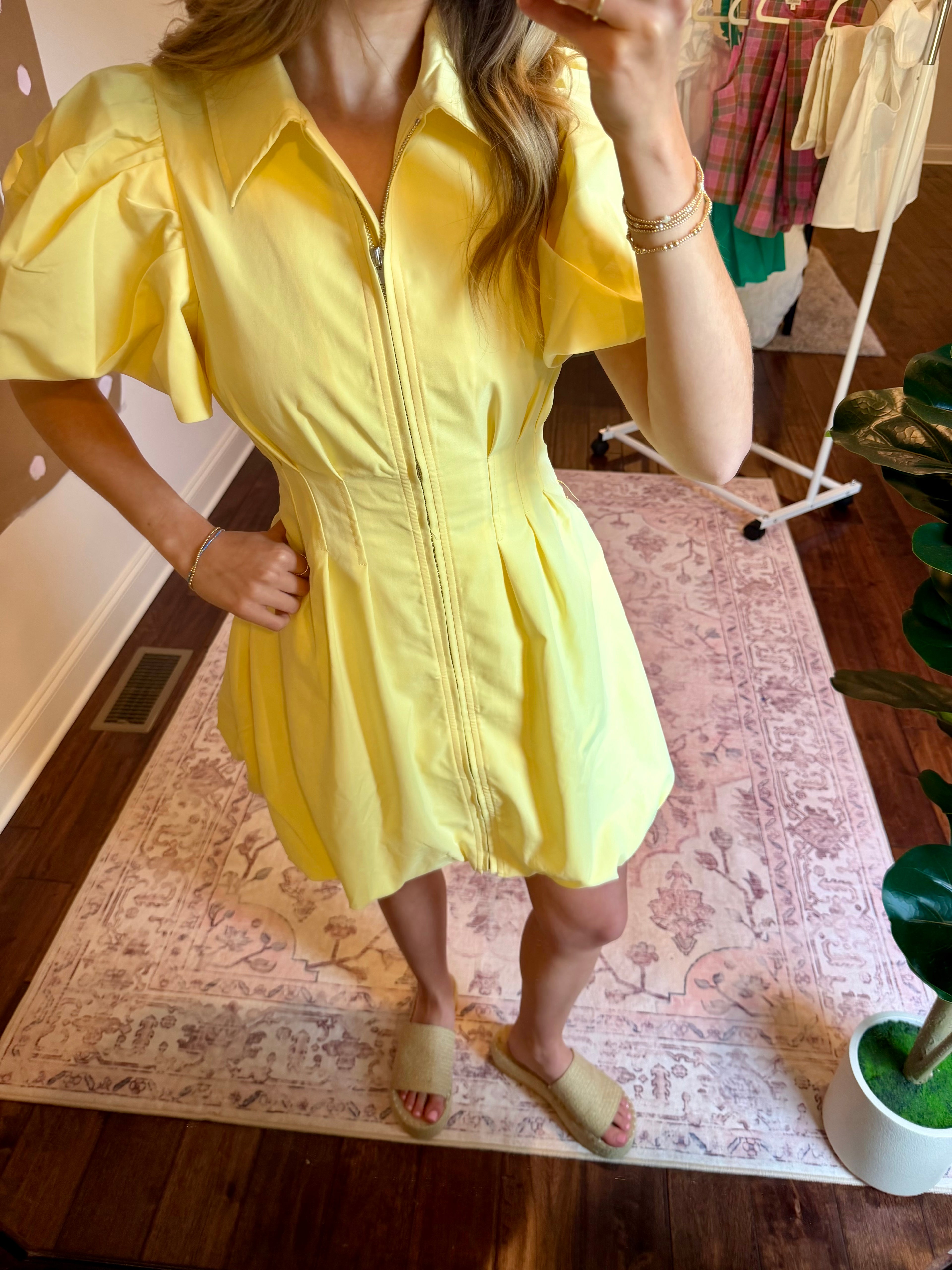 Person wearing a yellow dress in a room with a rug and plant.