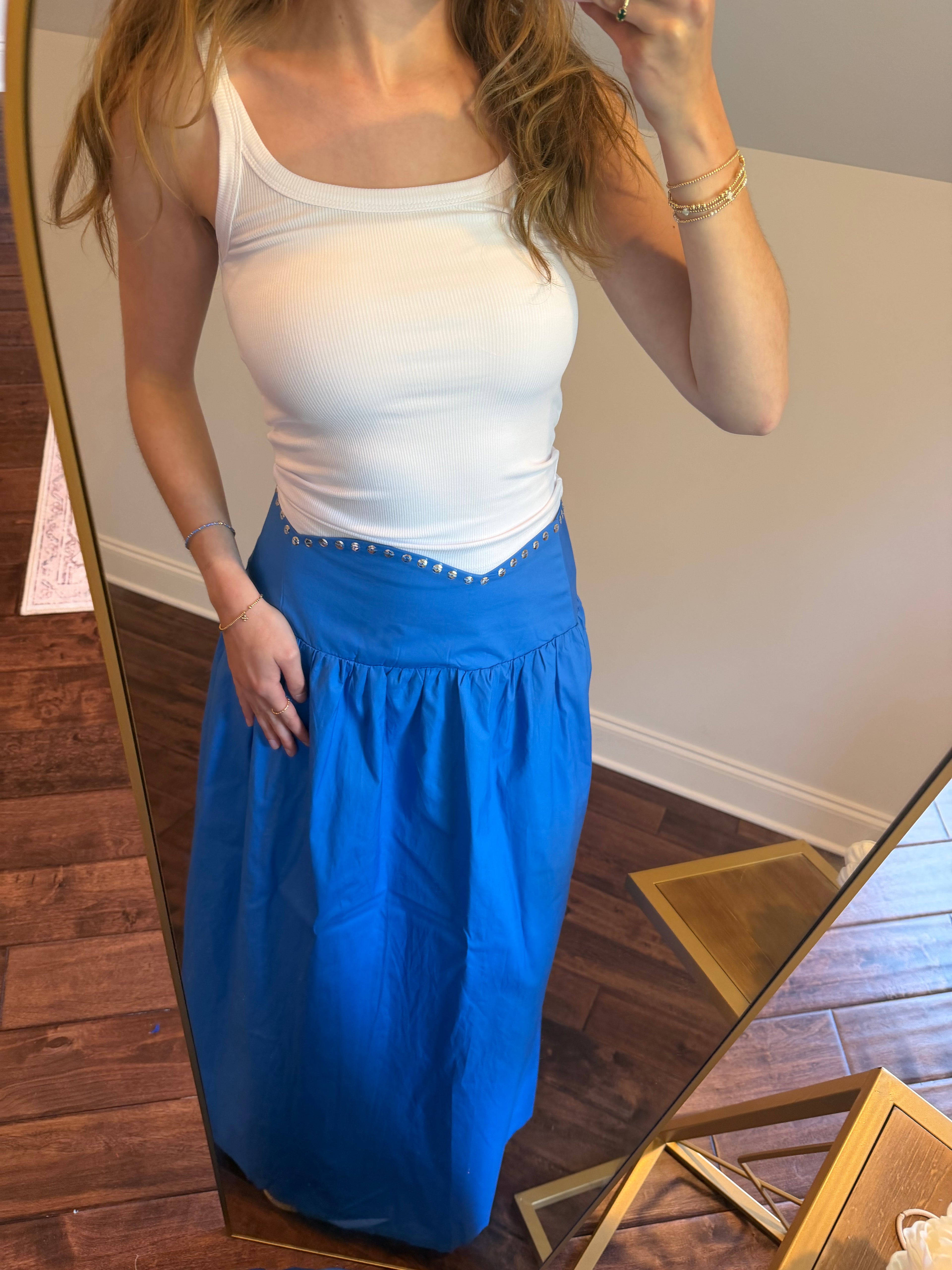 Woman wearing a white top and blue pants standing in front of a mirror.
