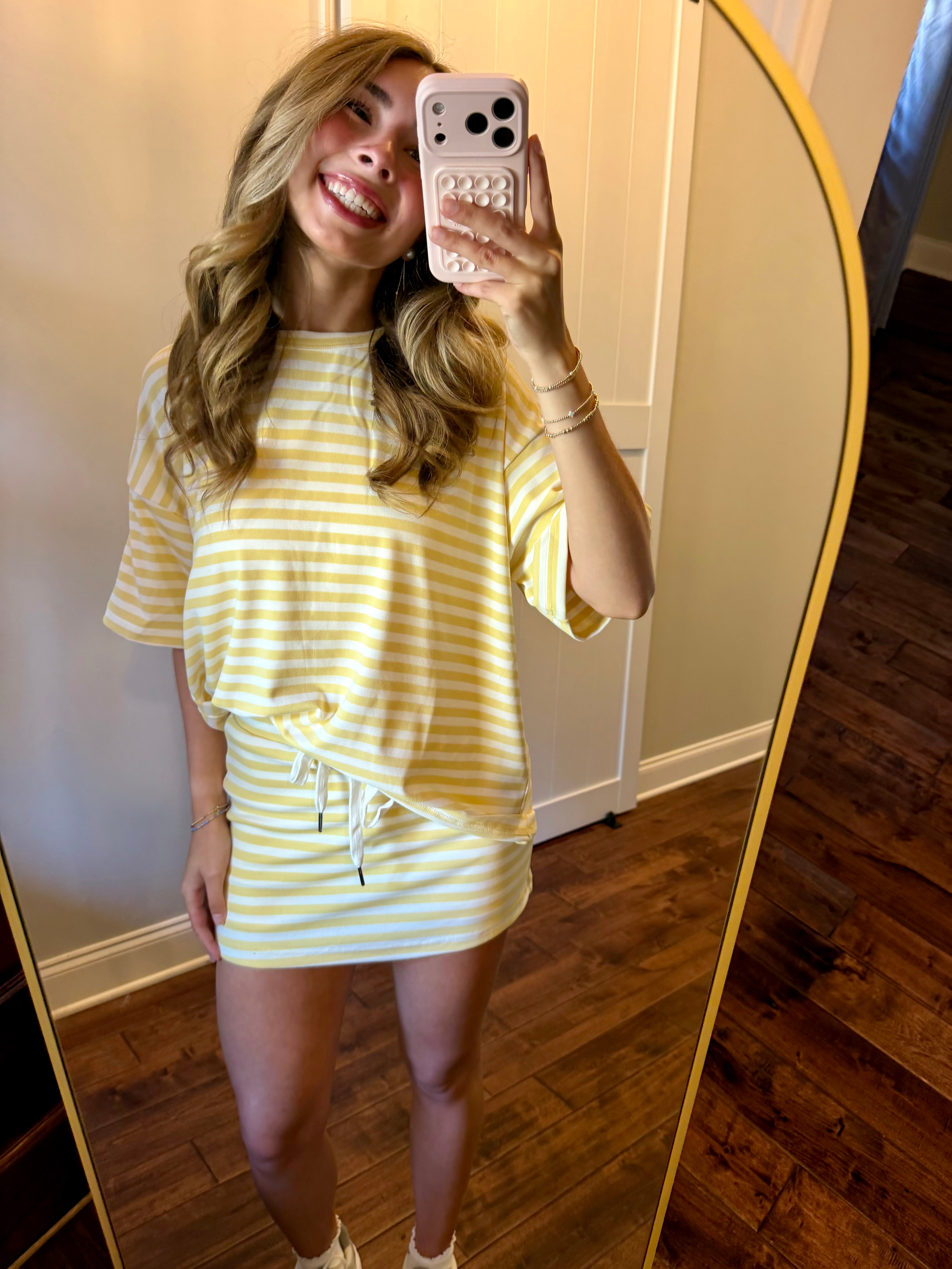 Woman taking a mirror selfie wearing a yellow and white striped dress.